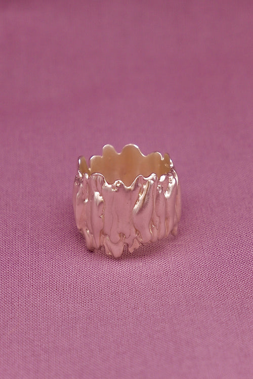 Silver ring with wavy design on a pink fabric background