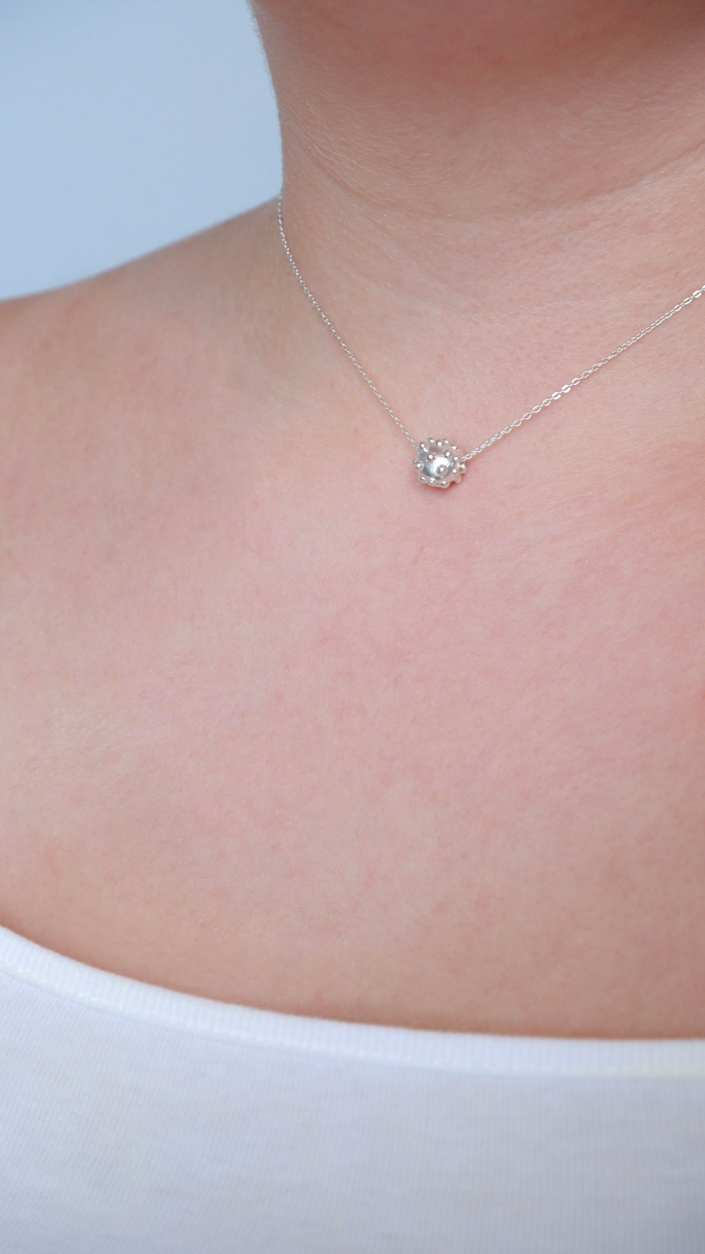Necklace with a small pendant on a person wearing a white top against a light background
