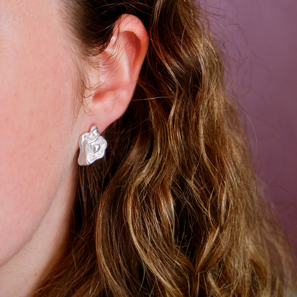 Close-up of a person wearing a silver earring with a pink background