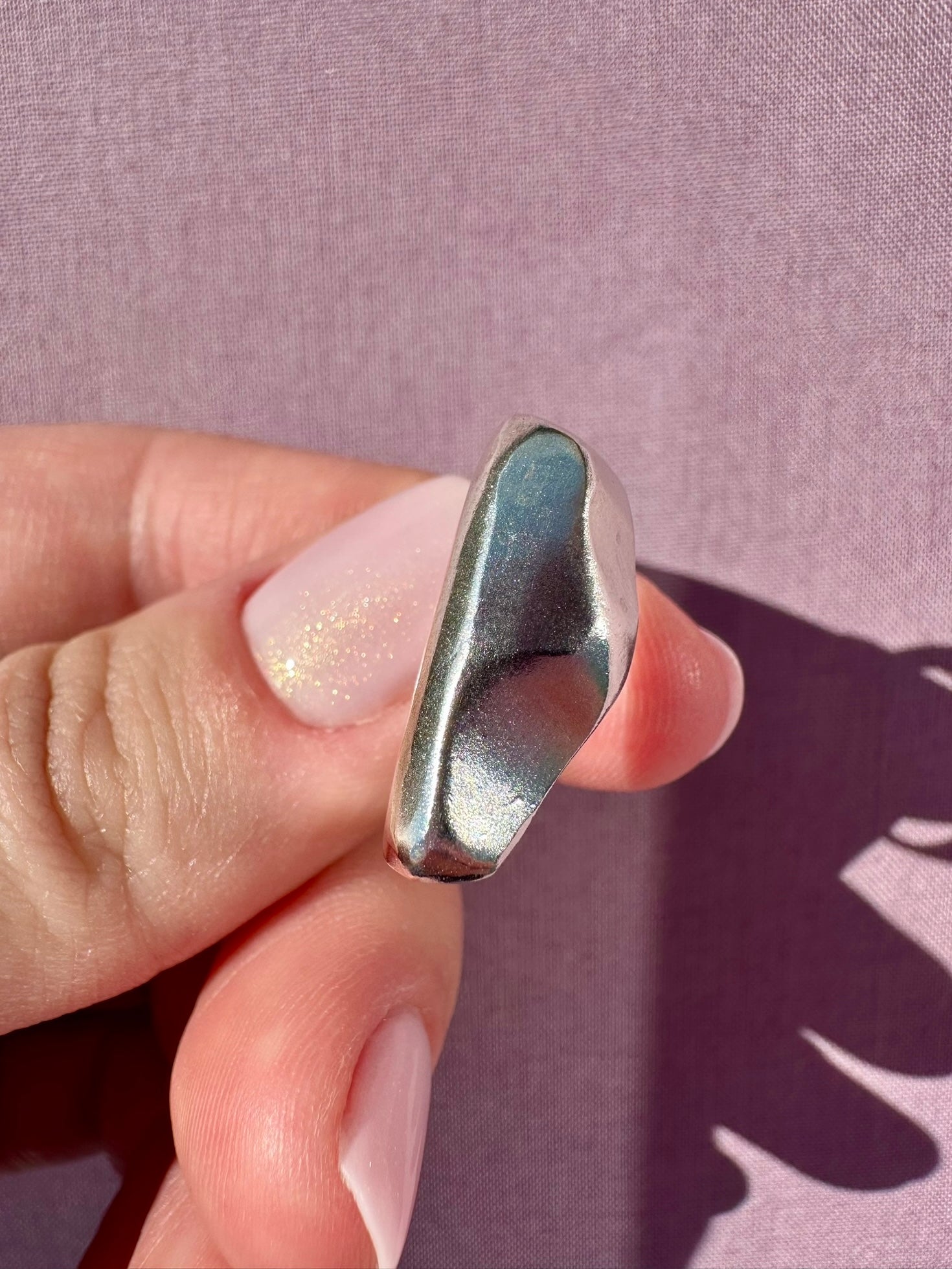 Silver ring held between fingers against a purple background