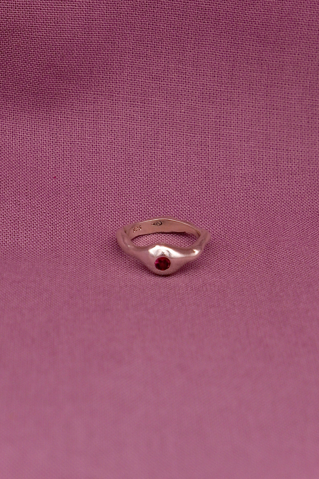 Silver ring with a red gemstone on a pink fabric background