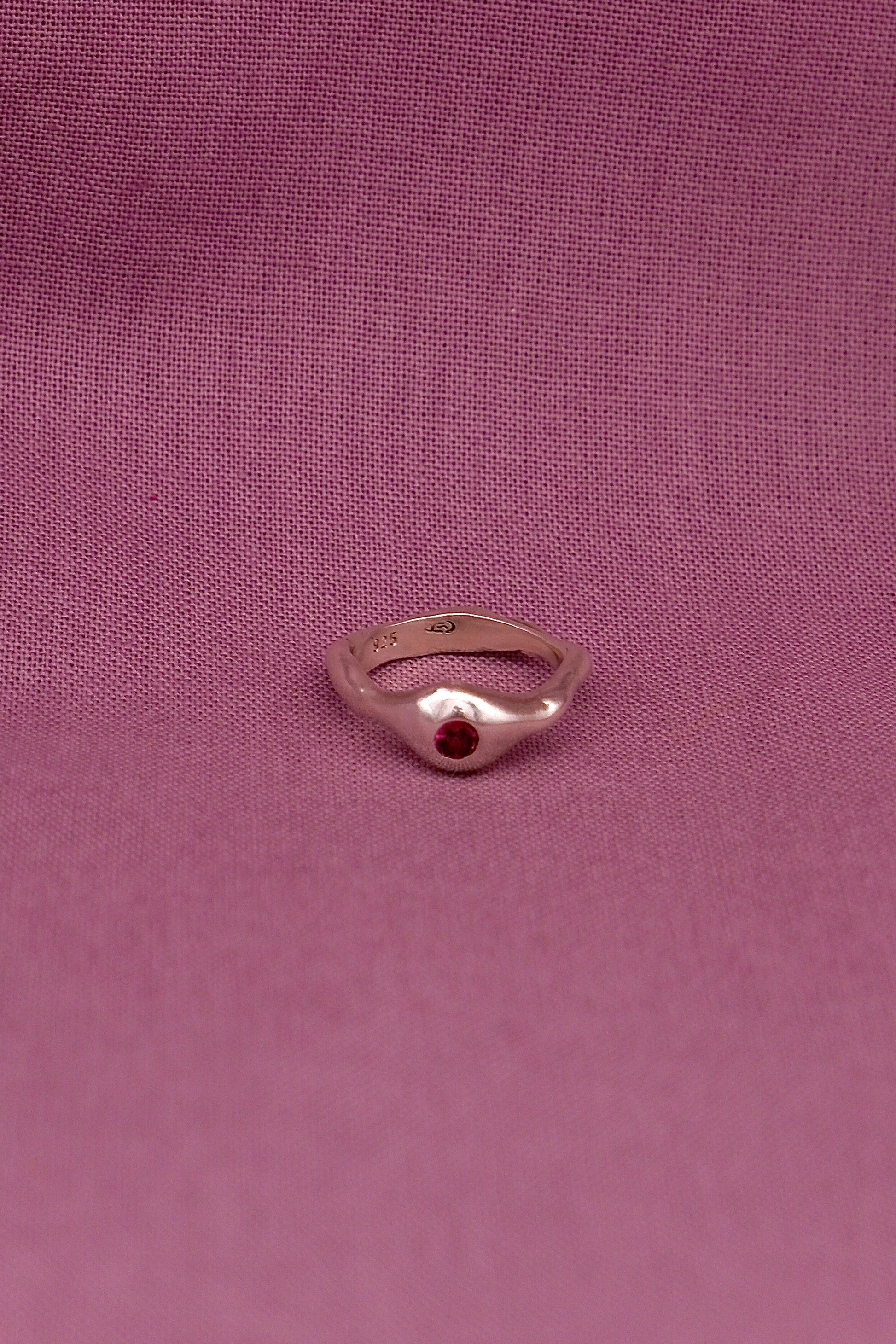 Silver ring with a red gemstone on a pink fabric background