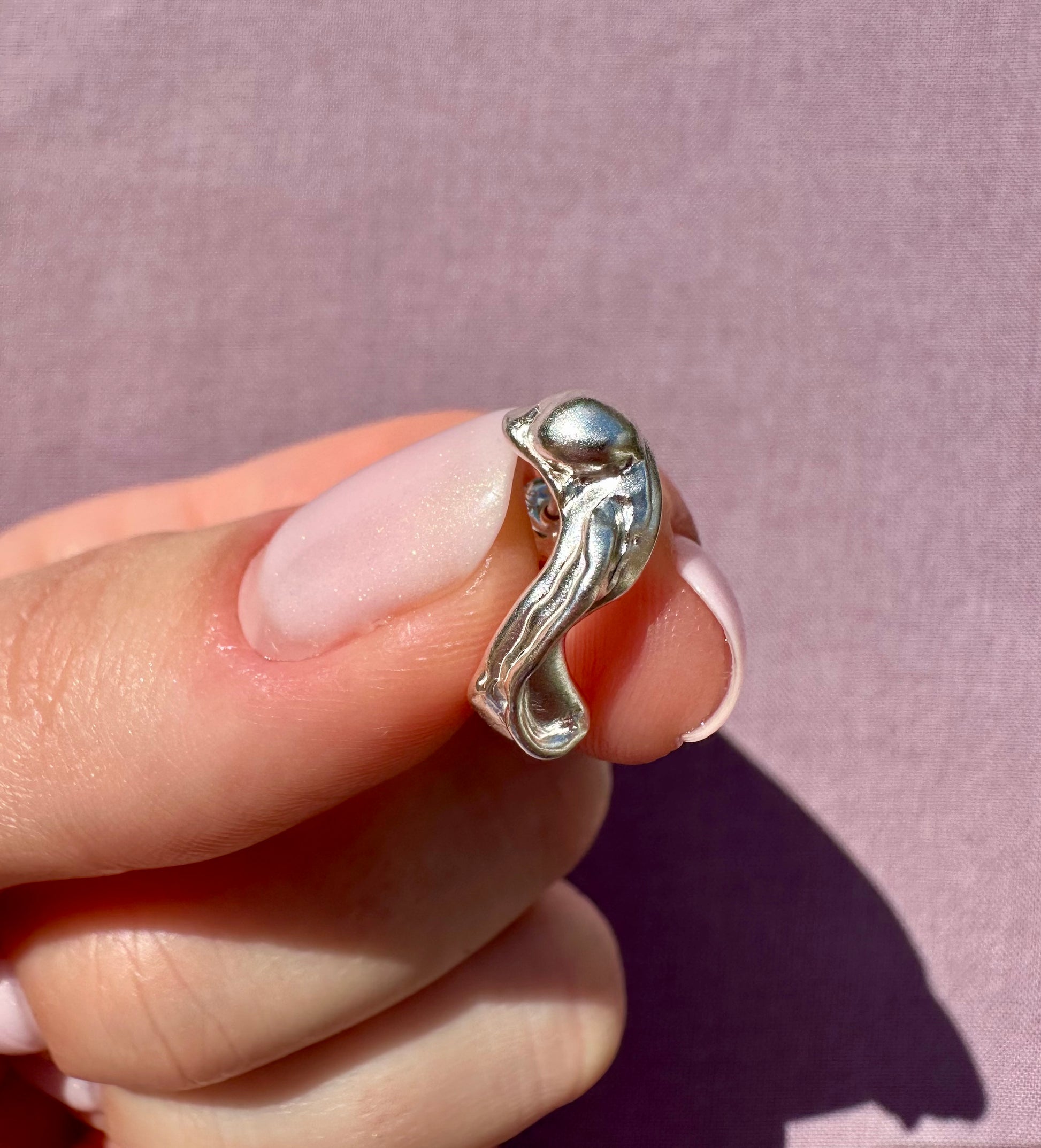 Silver earring with a unique design held between fingers against a pink background