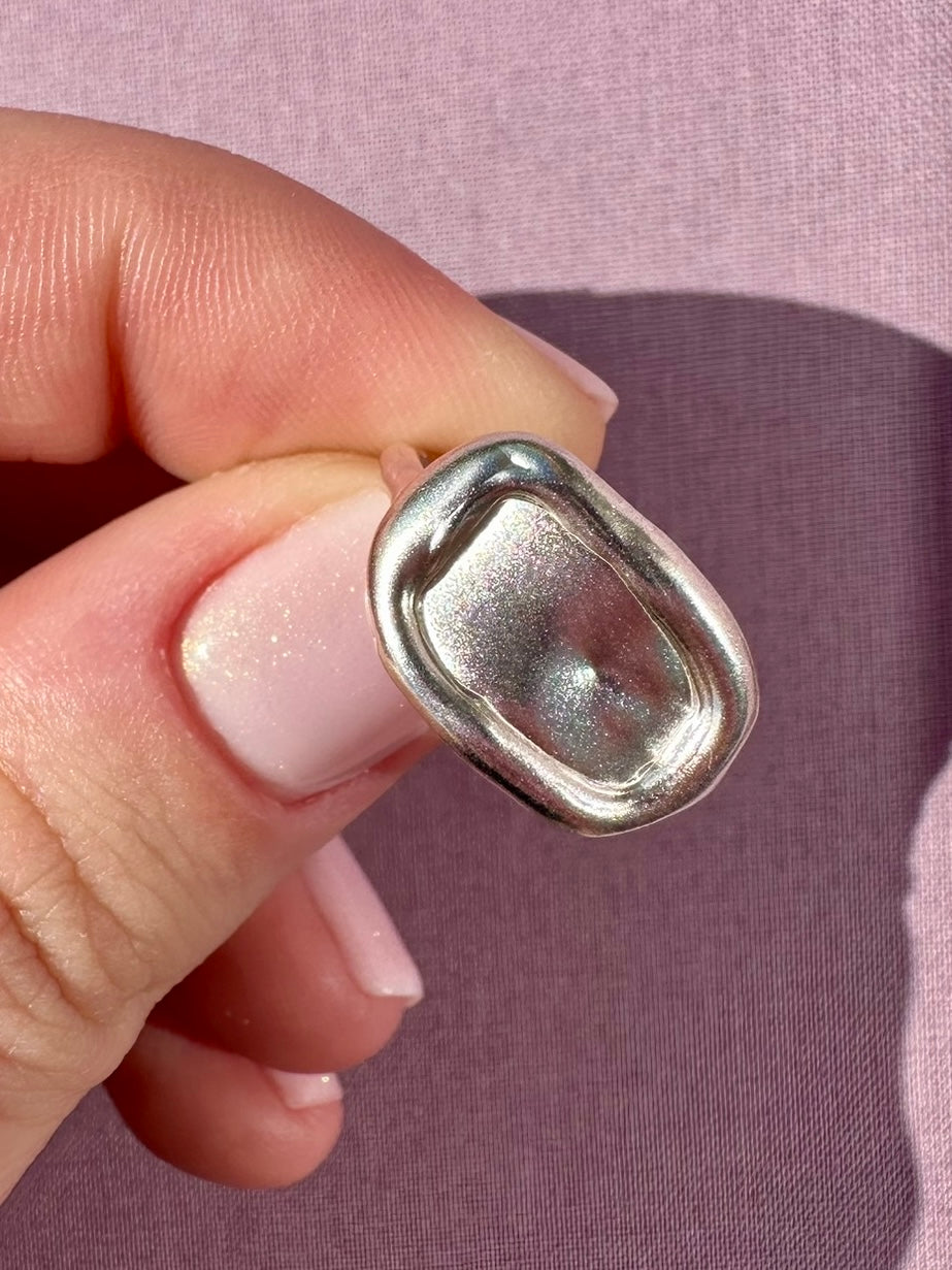 Silver ring held between fingers against a pink background
