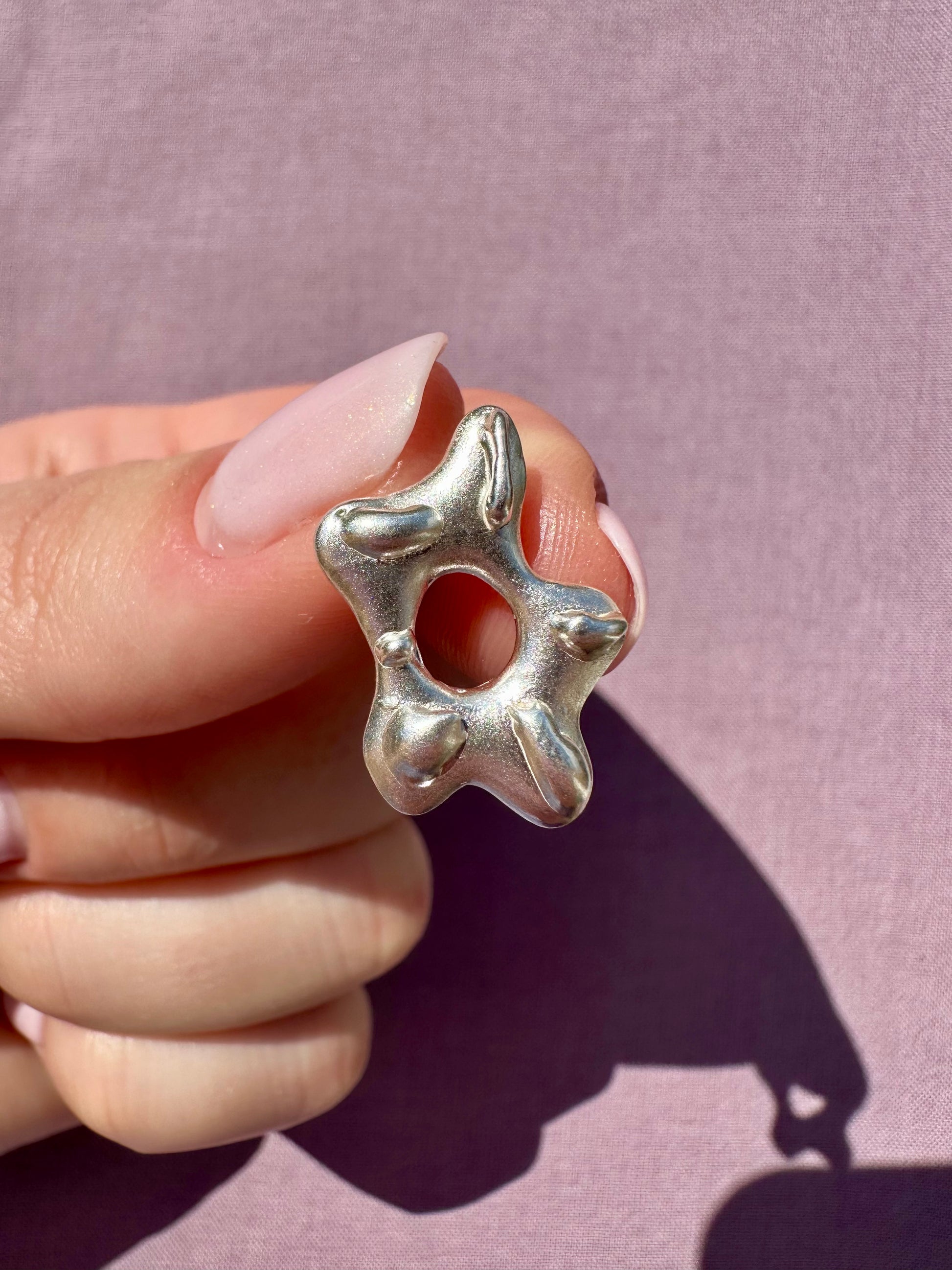 Silver earring held by a hand against a pink background