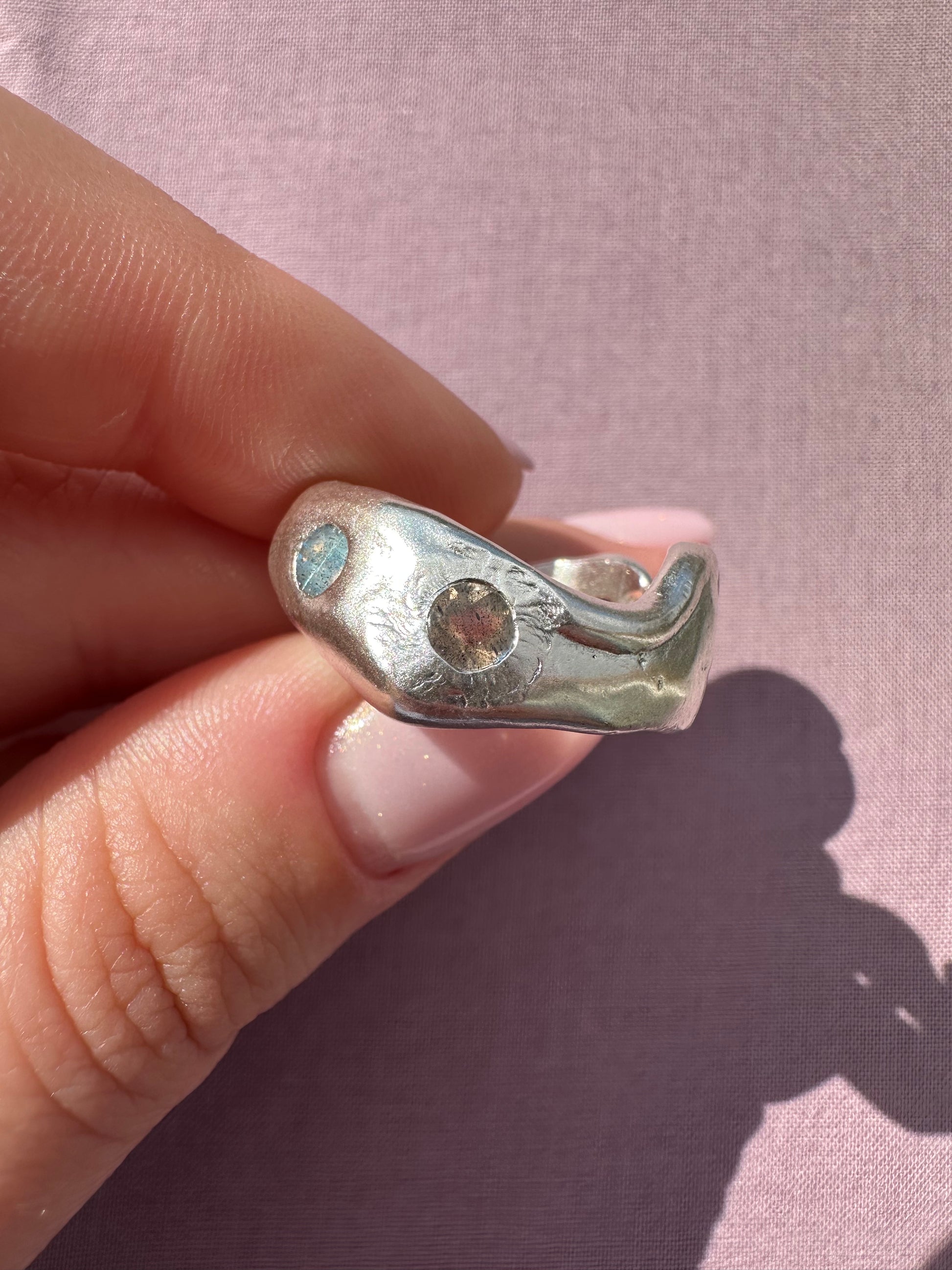 Silver ring with a gemstone held between fingers against a pink background