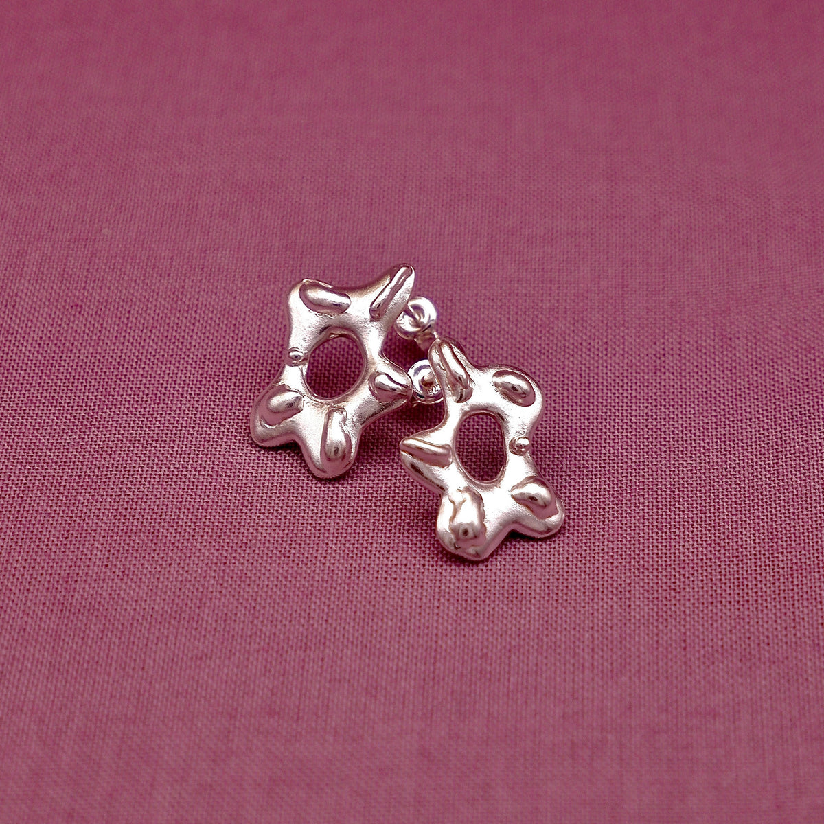 Silver earring on a pink fabric background