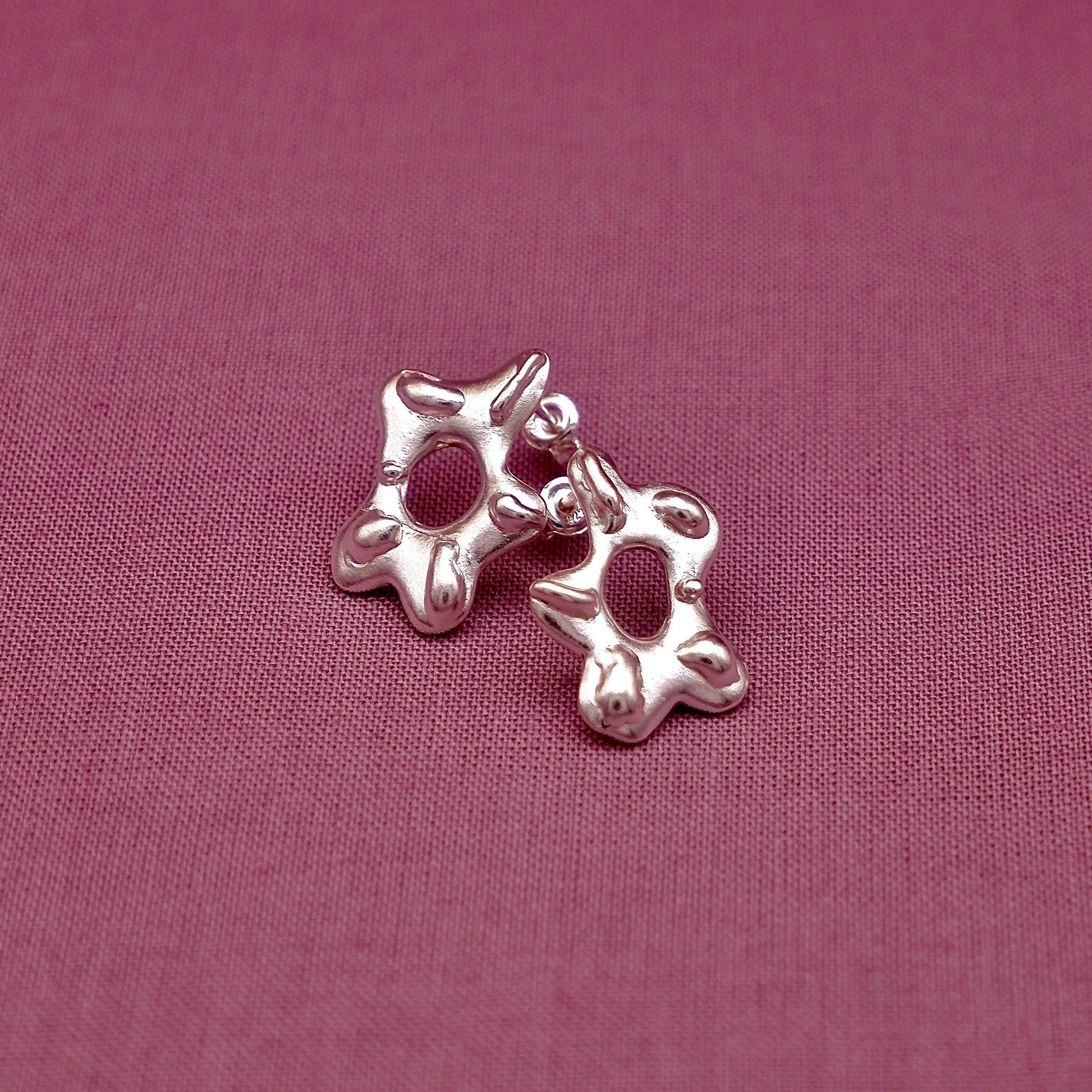 Silver earring on a pink fabric background