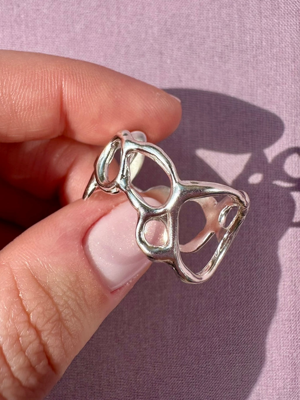 Silver ring held between fingers against a pink background