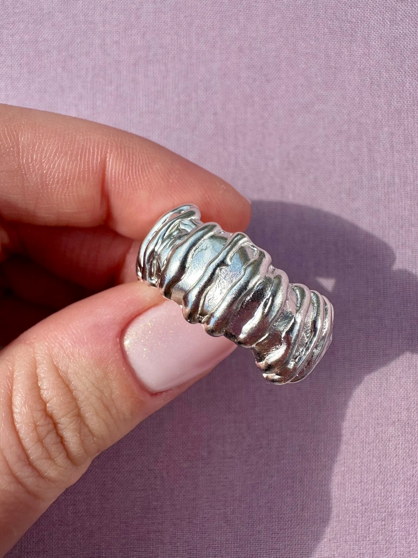 Silver ring held on a finger against a light purple background