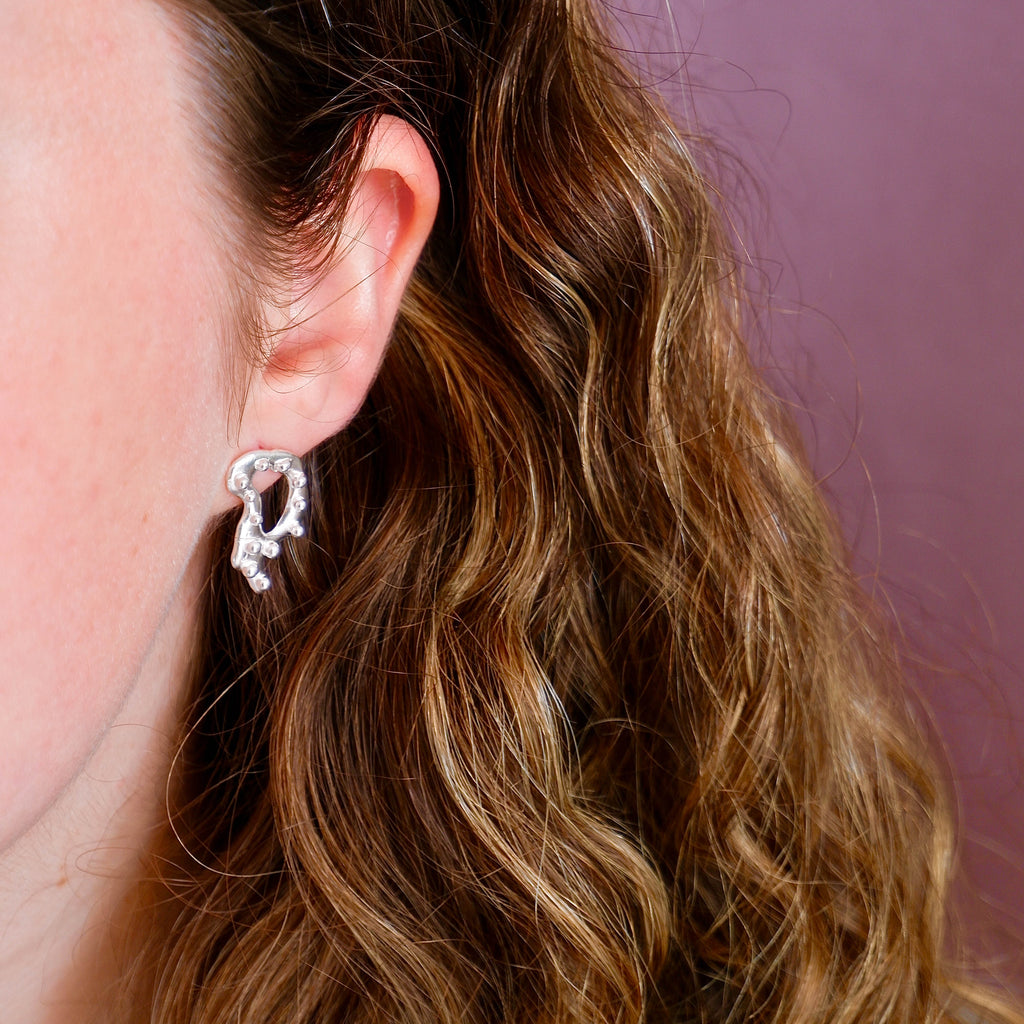 Close-up of an ear wearing a silver earring with a purple background