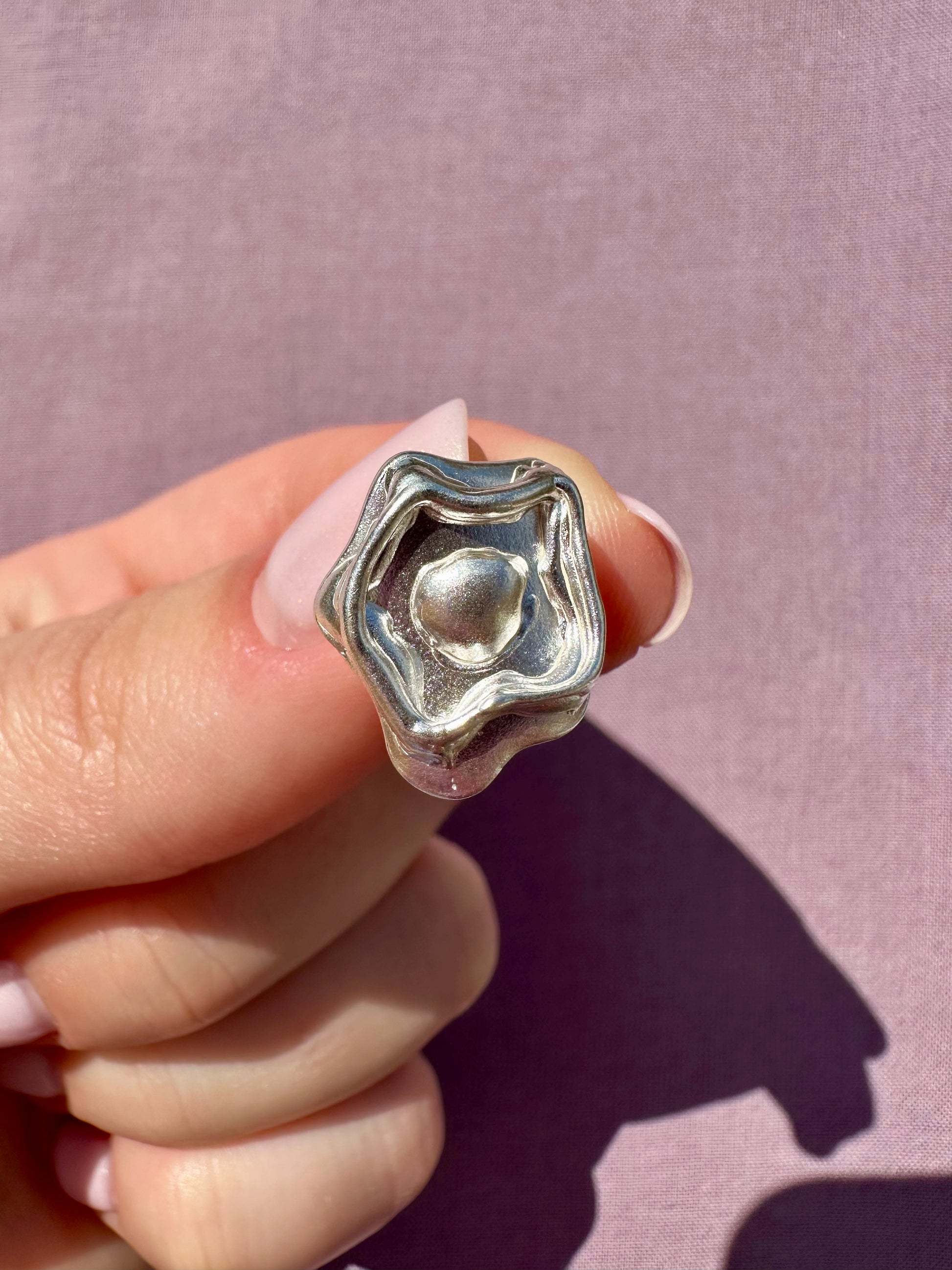 Silver earring held between fingers against a pink background