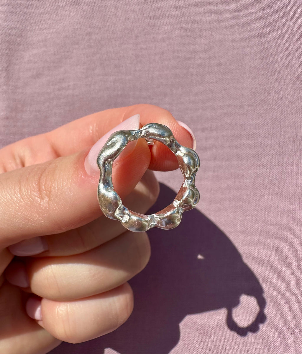 Silver earring held between fingers against a pink background
