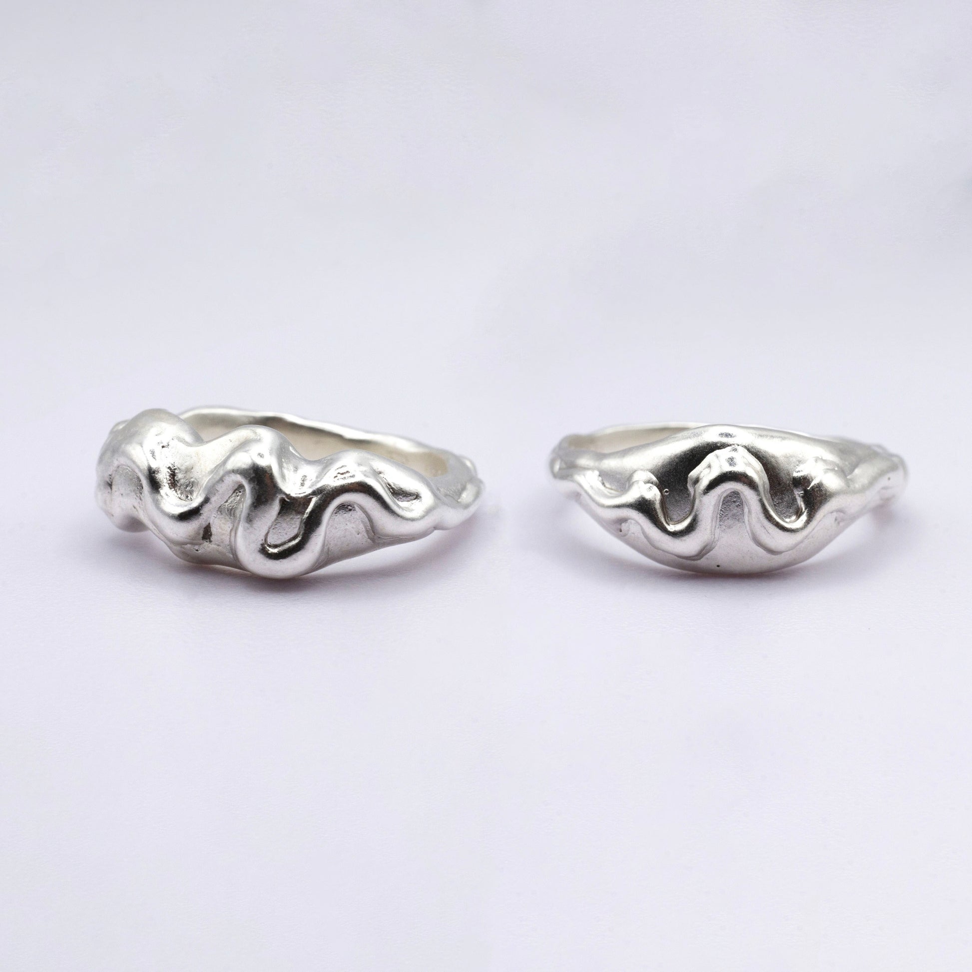 Pair of silver wave-shaped rings on a light gray background
