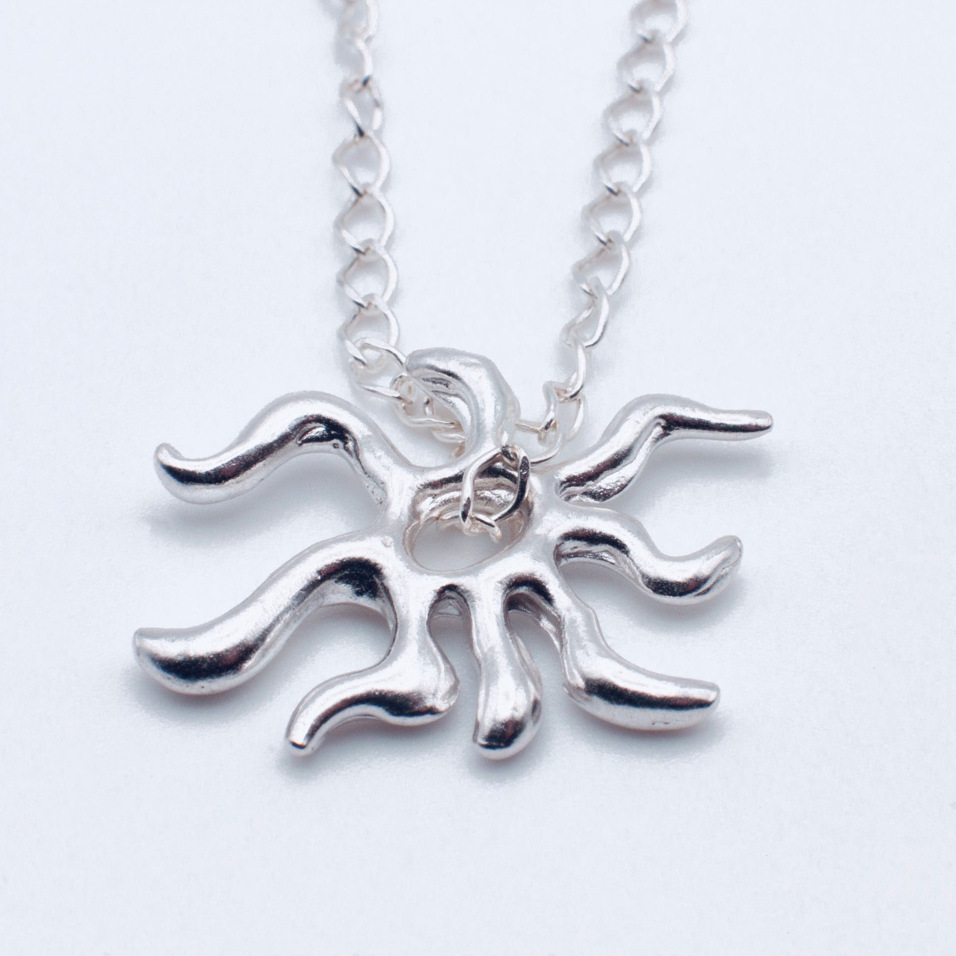 Silver sun-shaped pendant on a chain against a white background