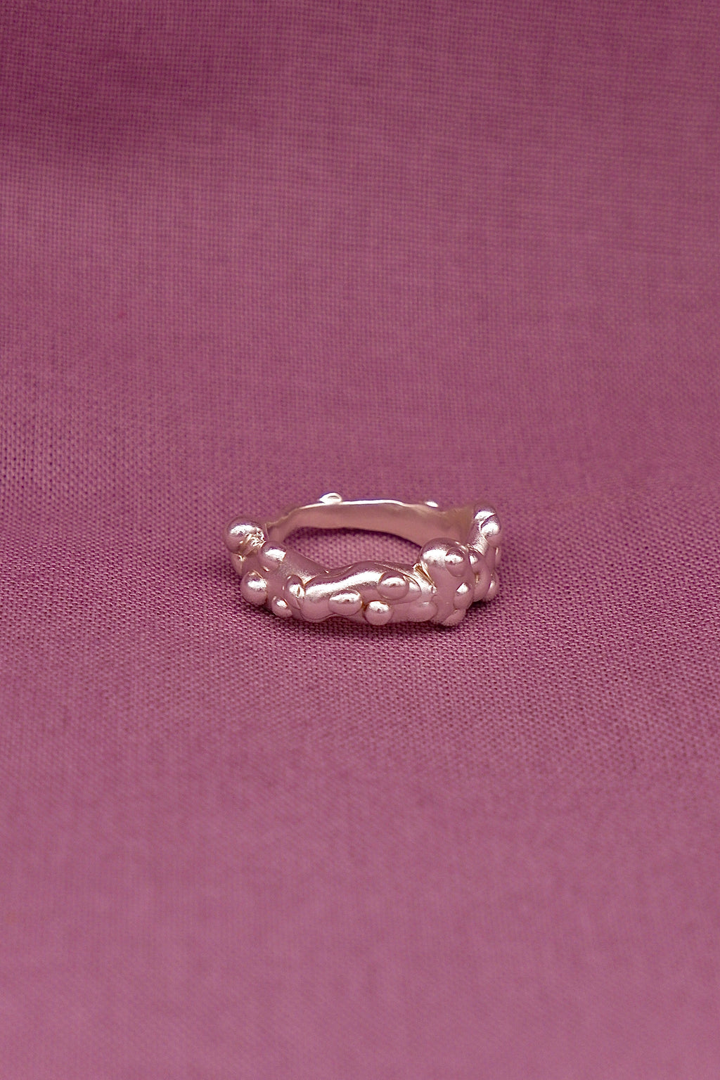 Silver ring with a textured design on a purple fabric background