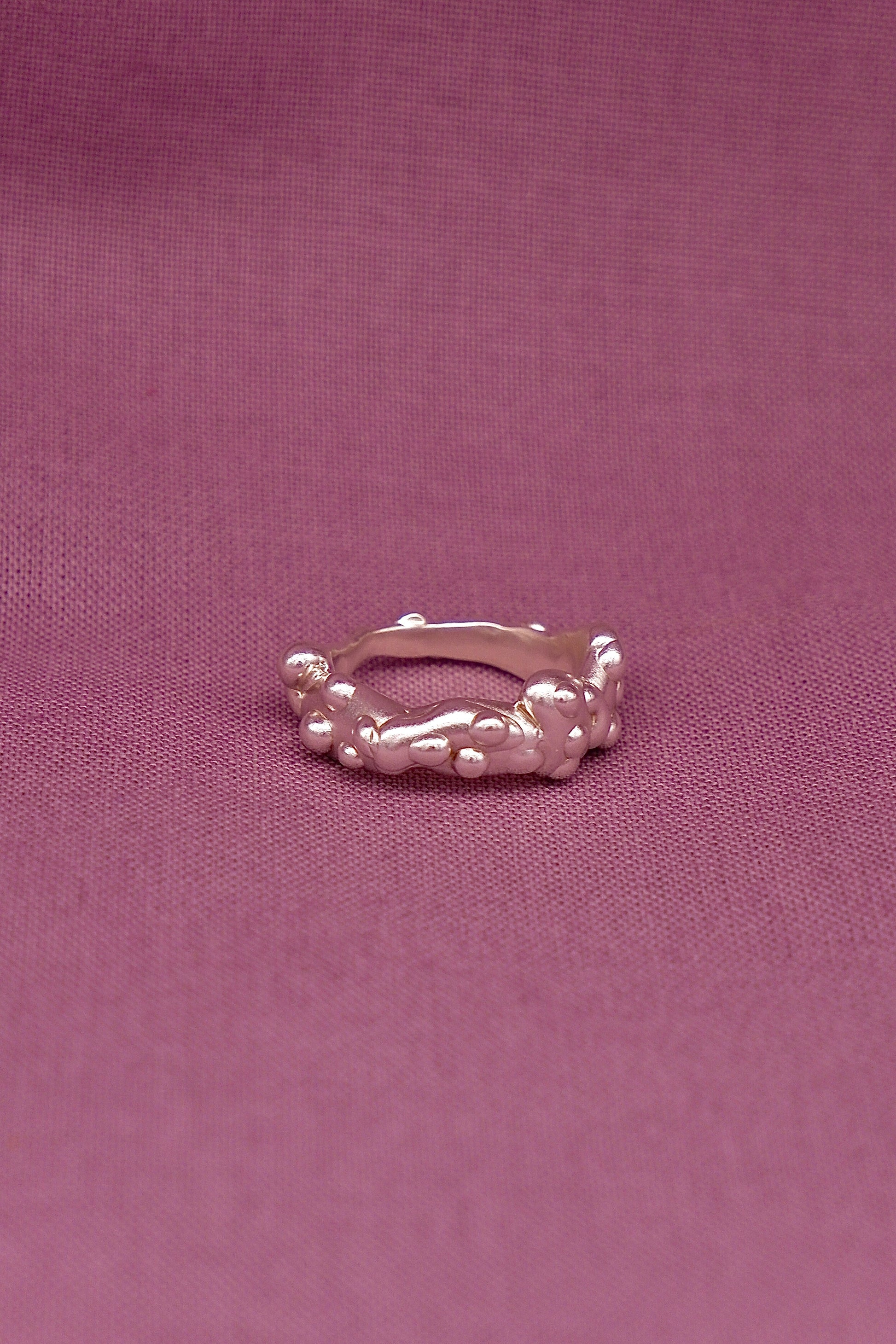 Silver ring with a textured design on a purple fabric background