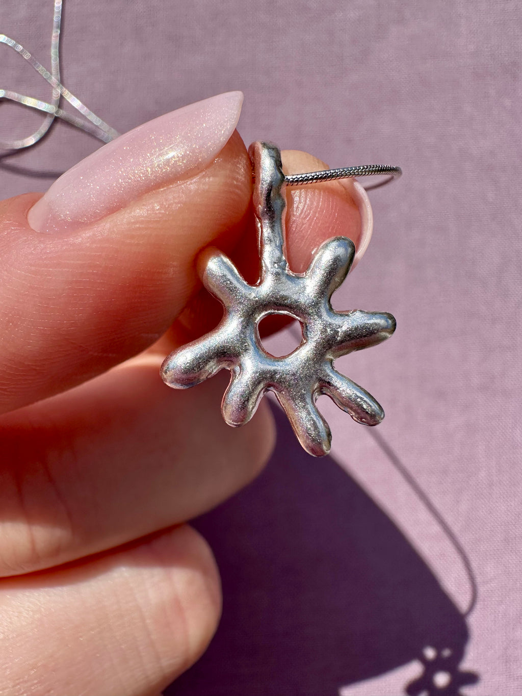 Silver star-shaped pendant held by a hand against a pink background