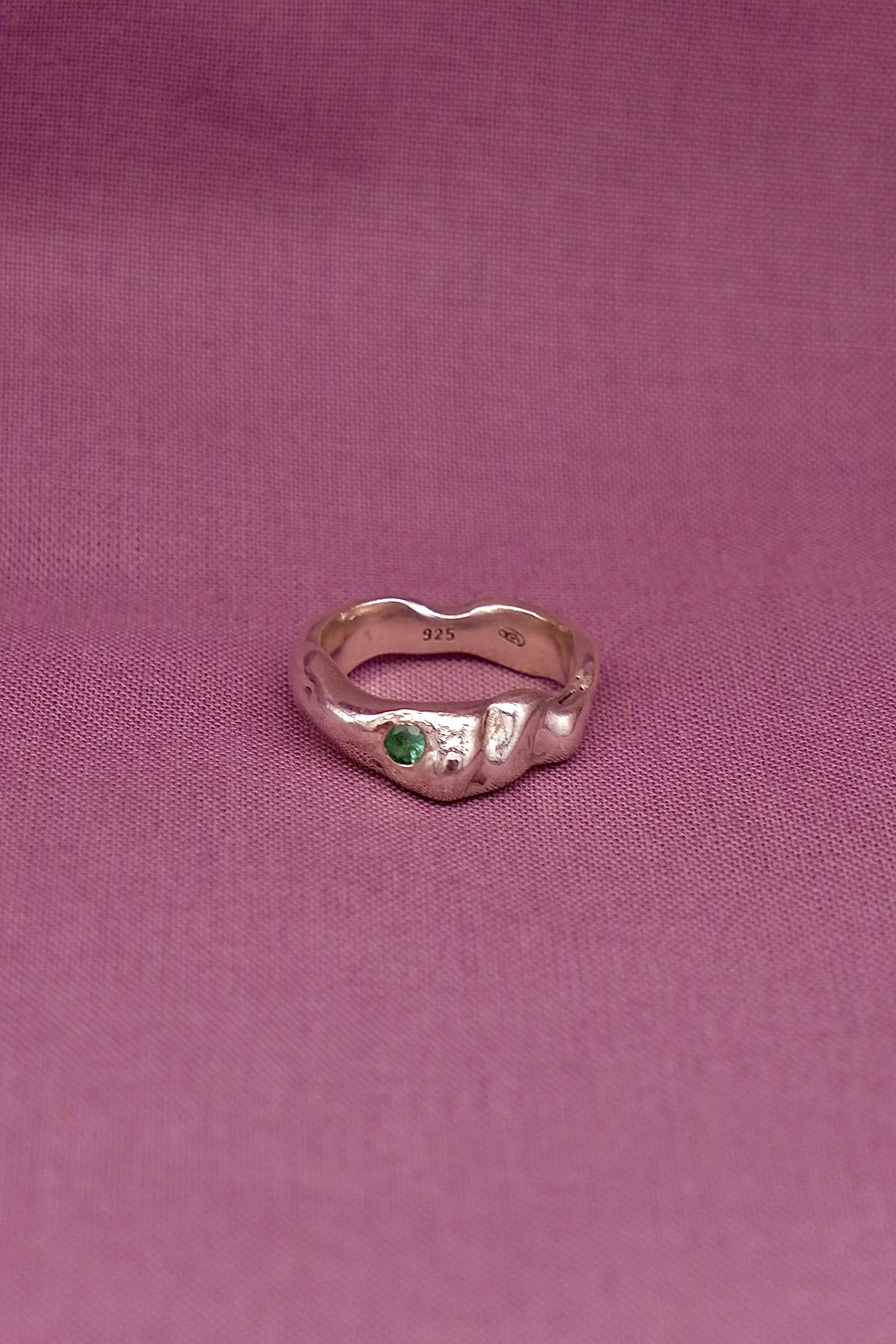 Silver ring with a green gemstone on a purple fabric background