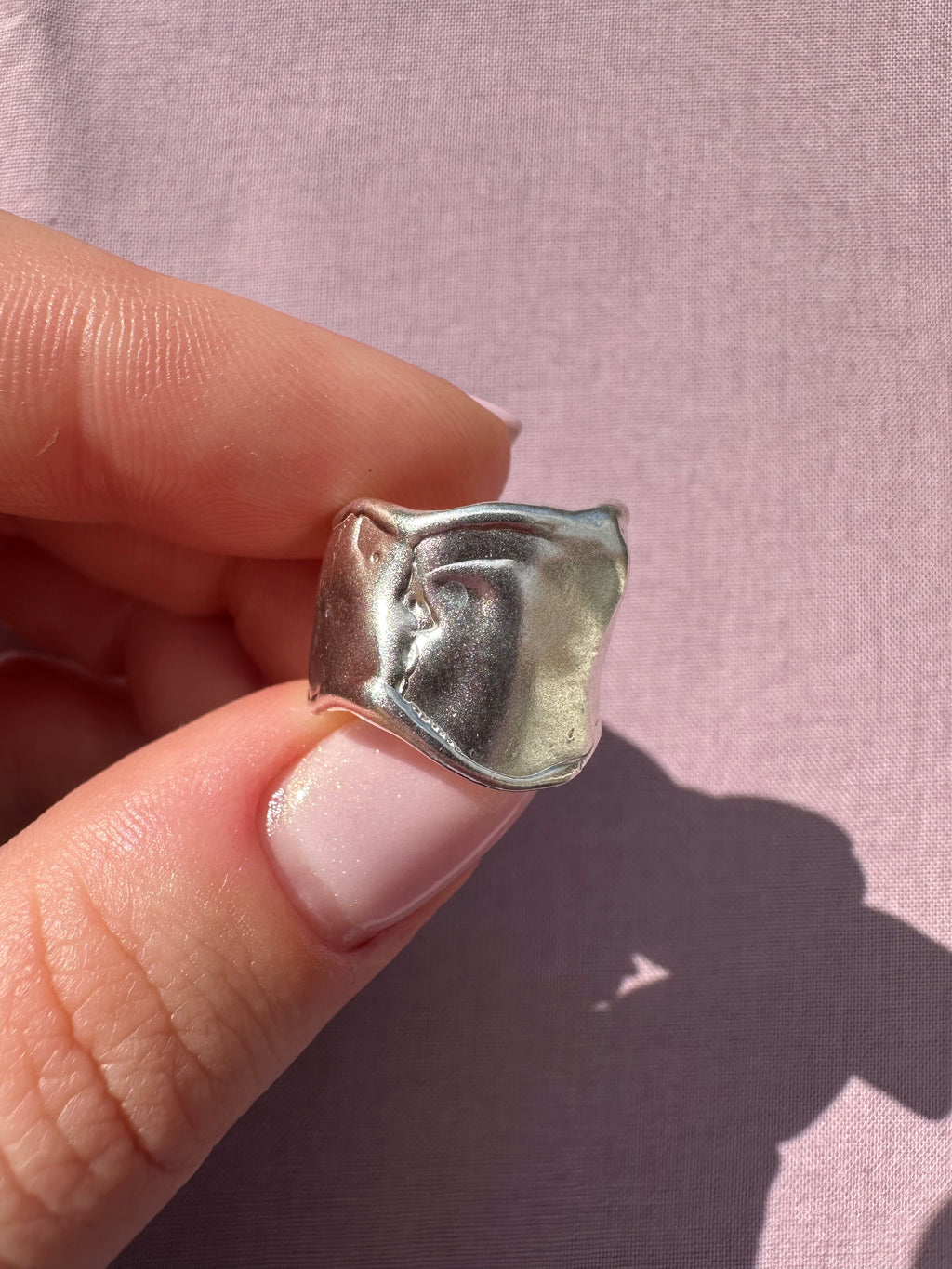 Hand holding a small silver ring against a pink background