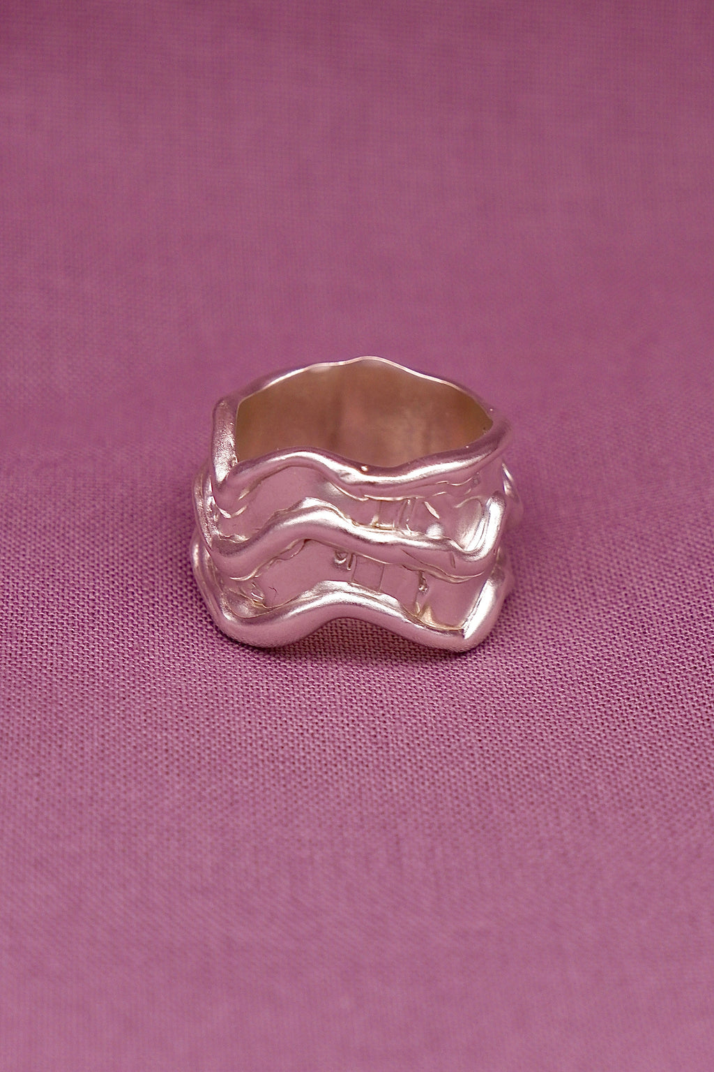 Silver ring with wavy design on a pink fabric background