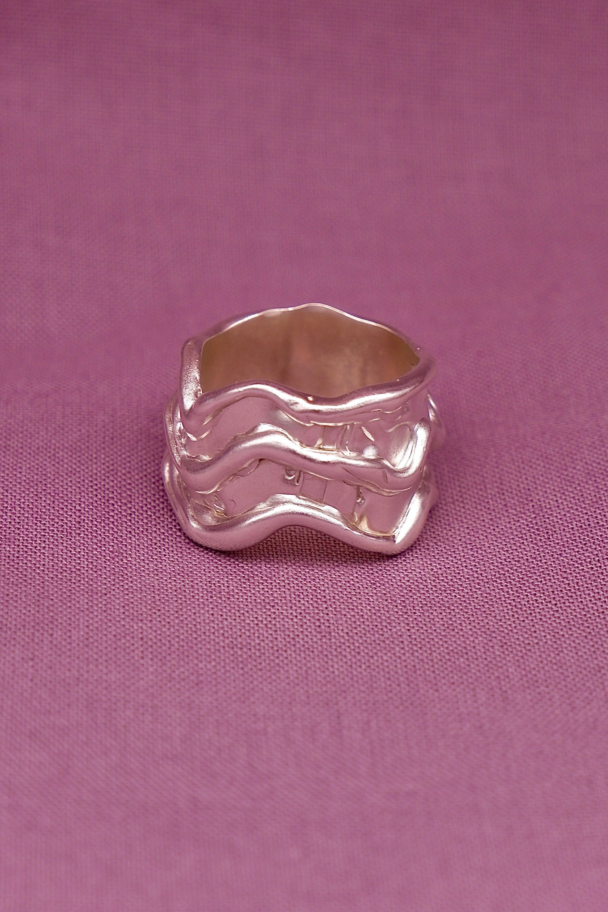 Silver ring with wavy design on a pink fabric background