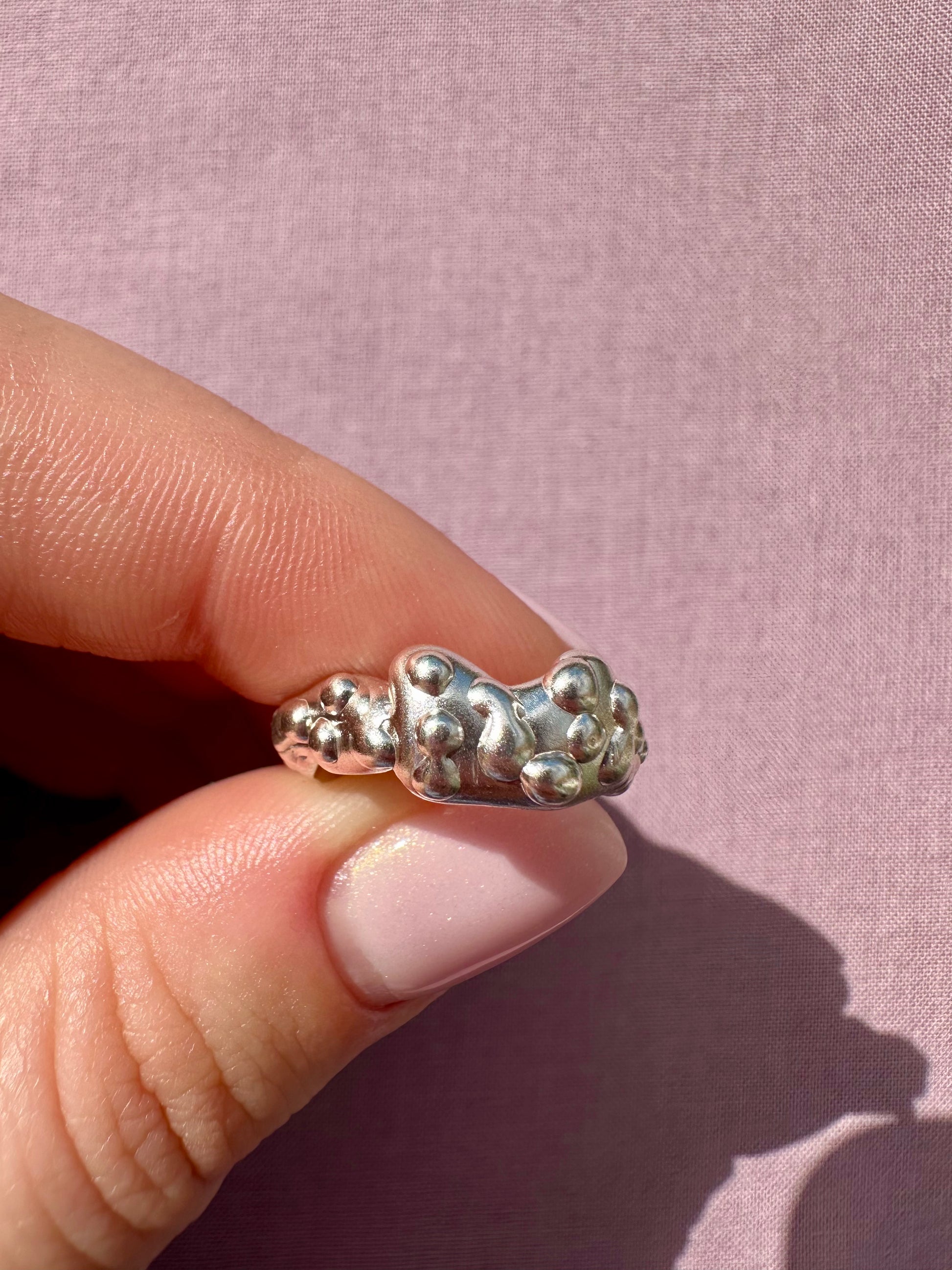 Silver ring with a textured design on a pink background