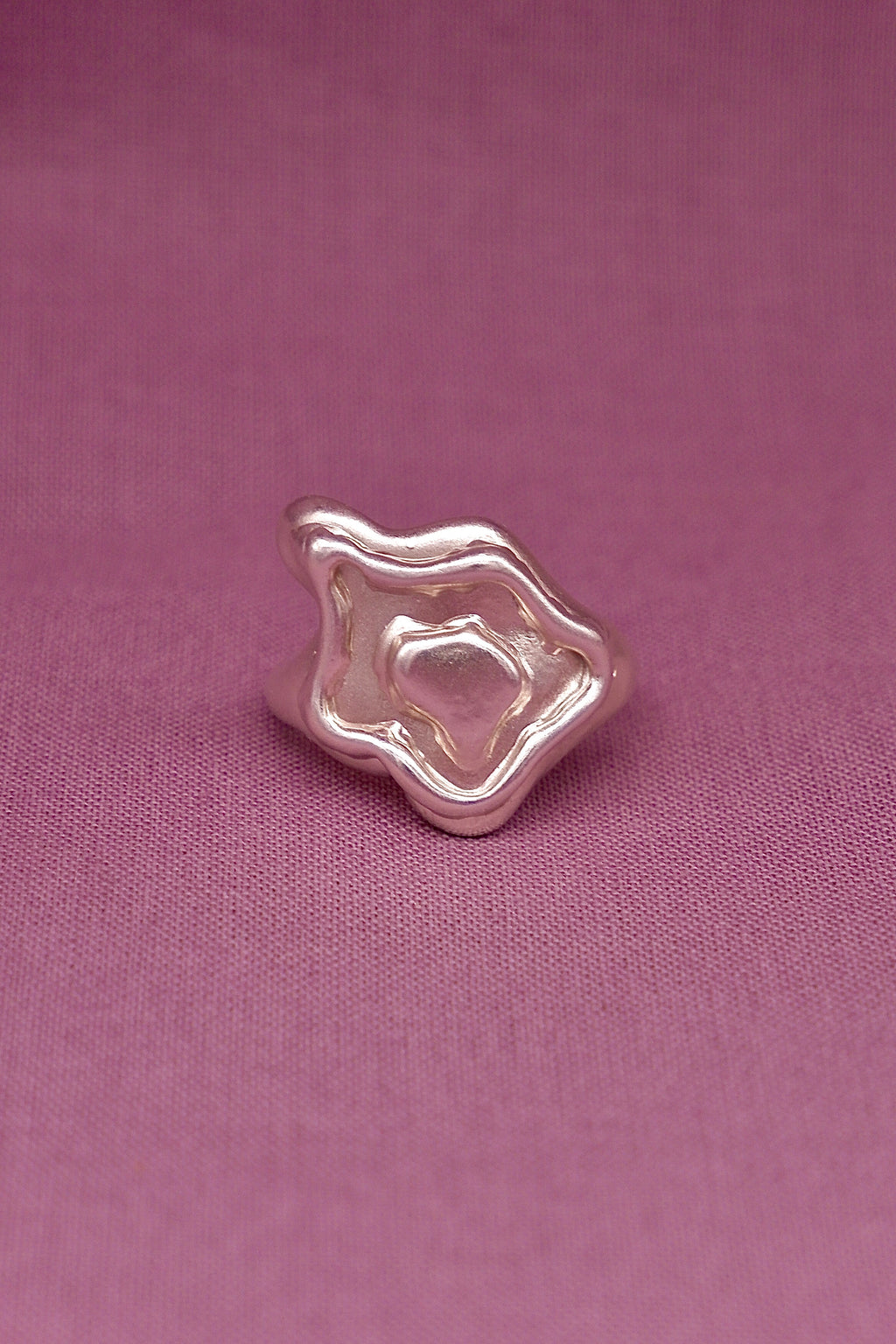 Silver ring with a unique design on a pink fabric background