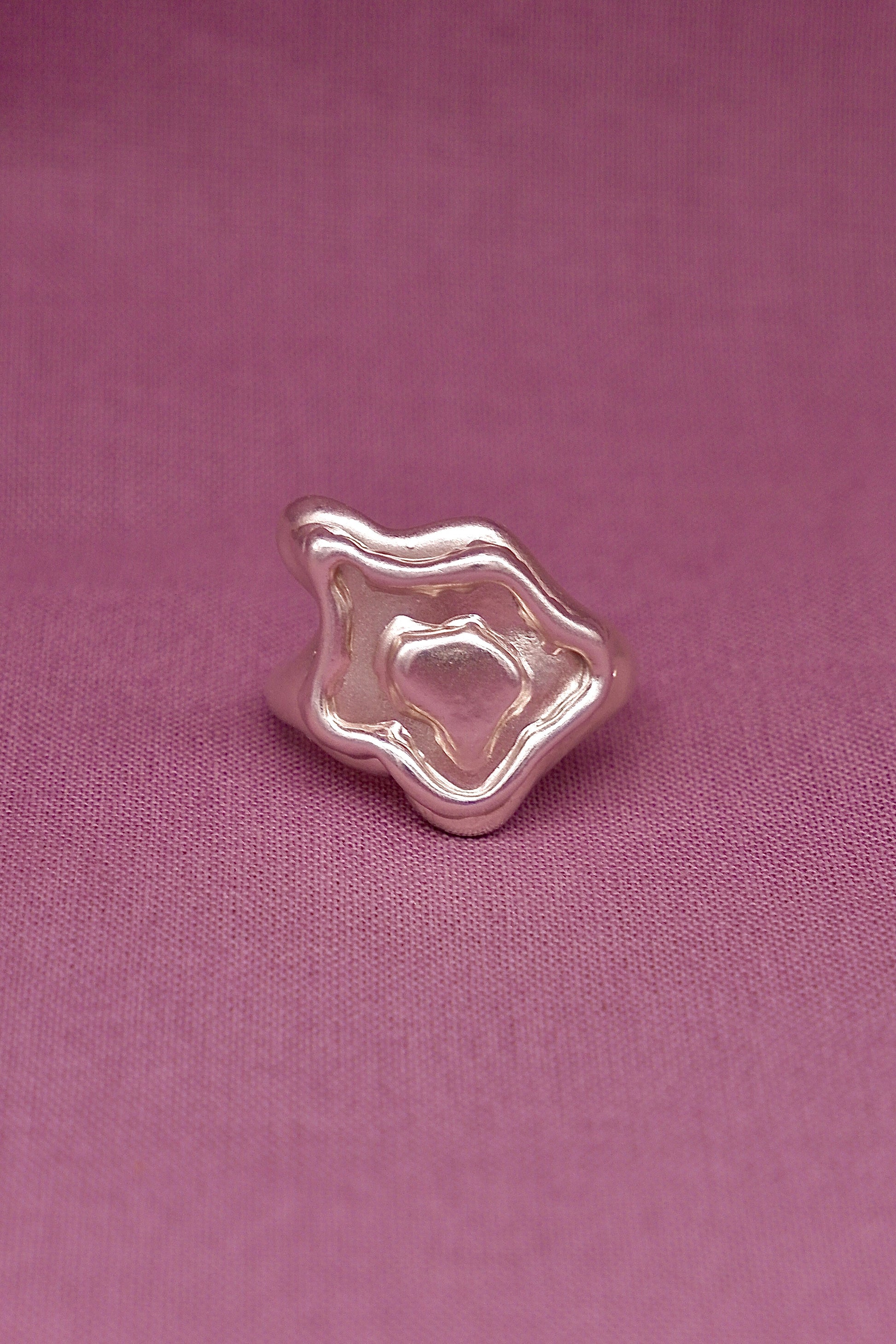 Silver ring with a unique design on a pink fabric background