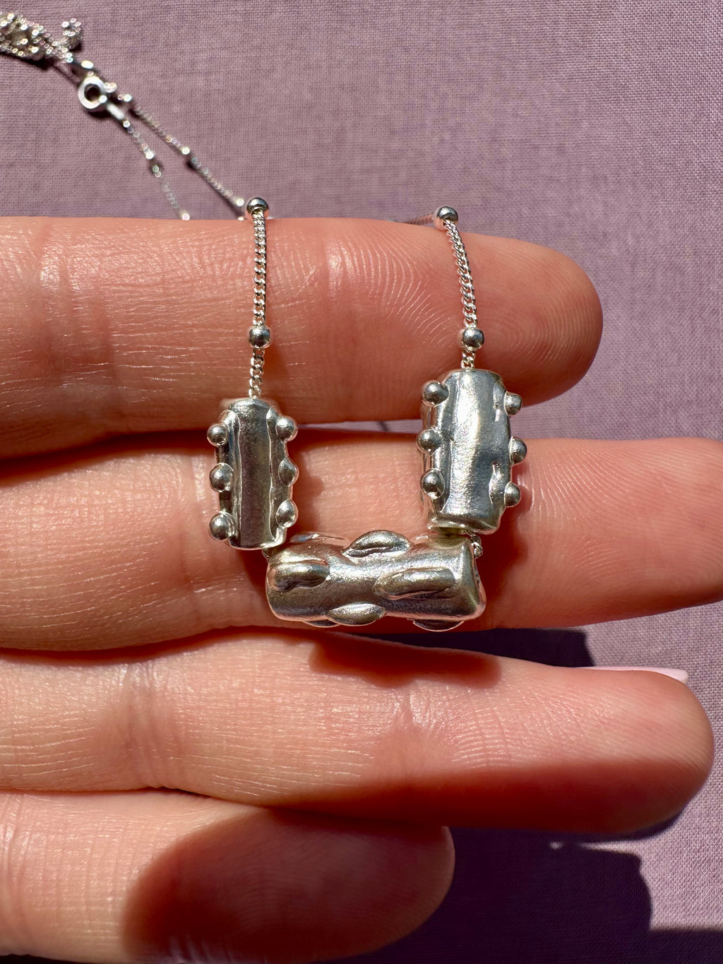 Silver necklace with a unique pendant held between fingers against a purple background