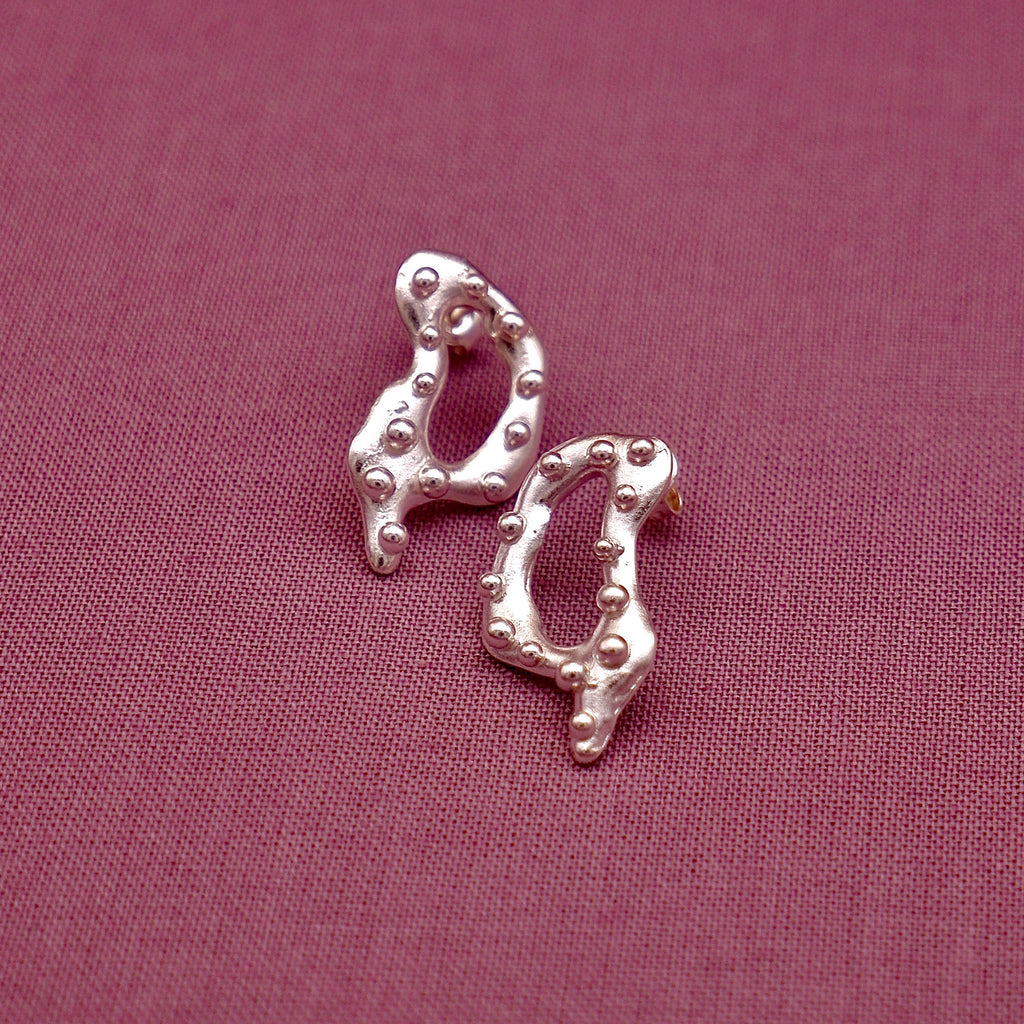 Silver earrings on a pink fabric background