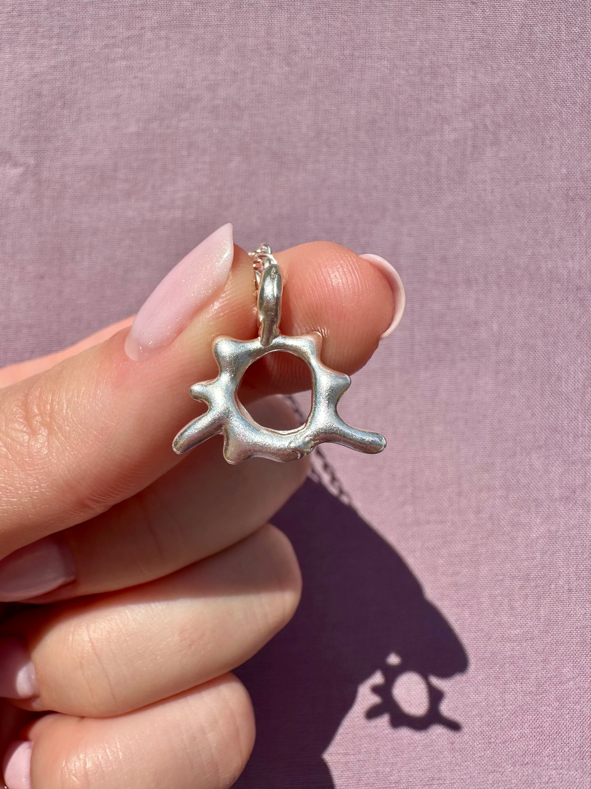 Silver star-shaped pendant held by a hand against a pink background