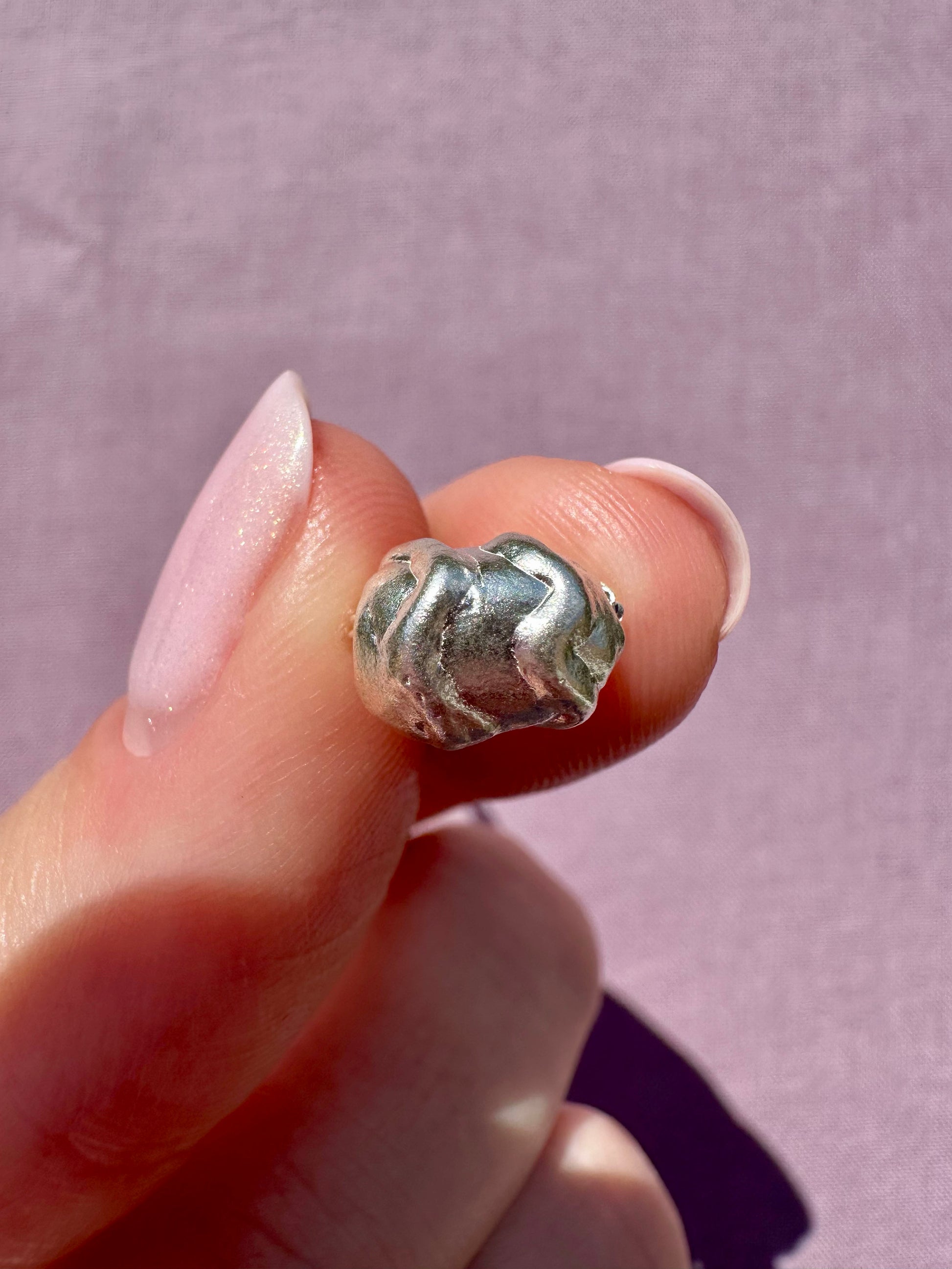 Silver beehive-shaped earring held between fingers against a light purple background