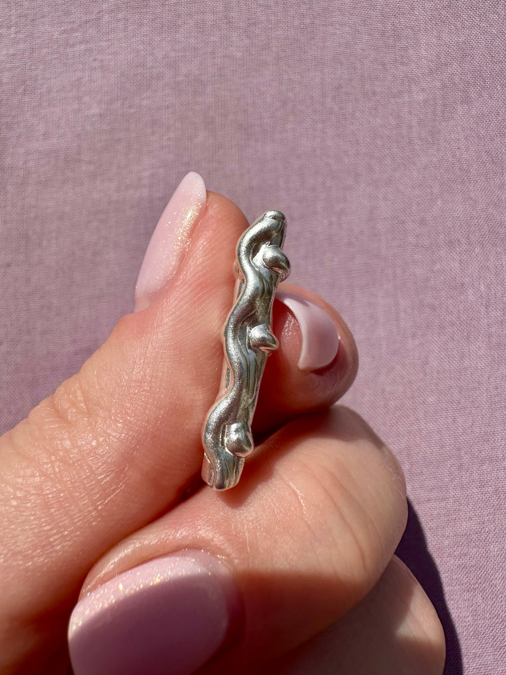 Silver bracelet with a unique design worn on a finger against a pink background
