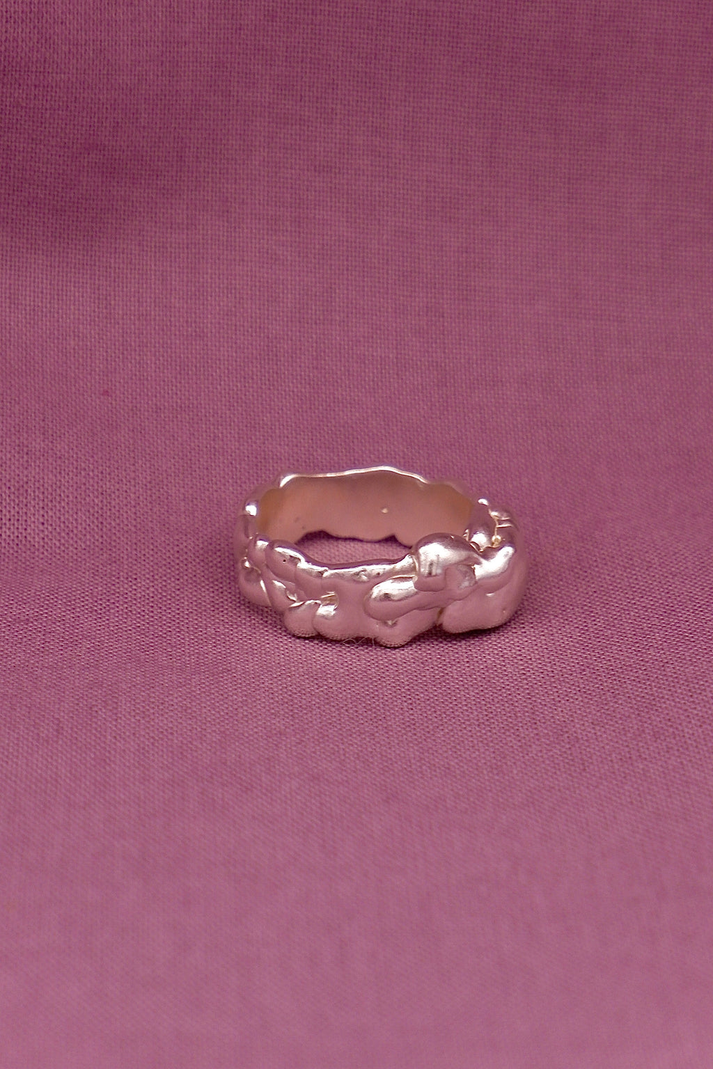 Silver ring with a textured band on a pink fabric background