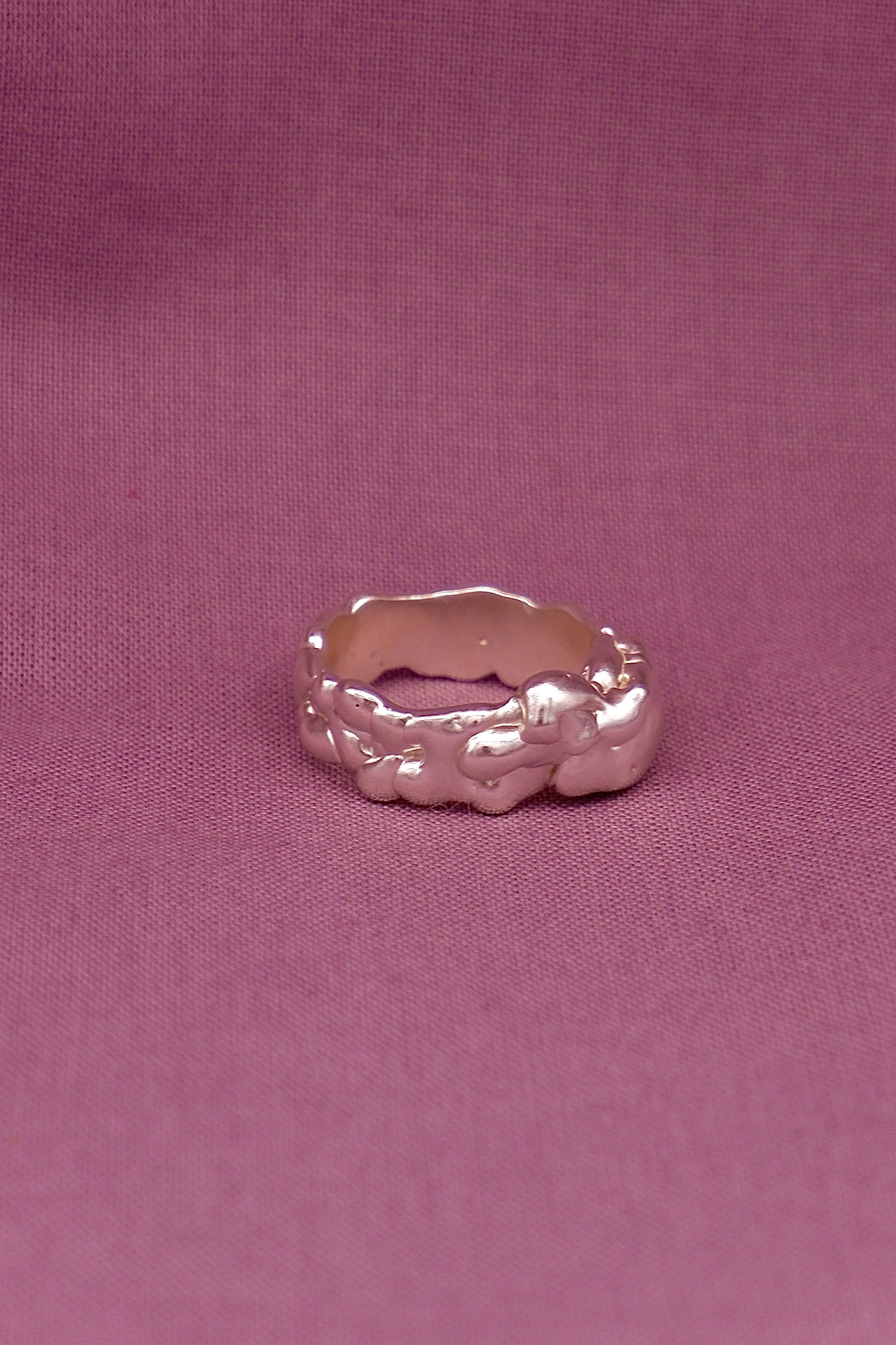 Silver ring with a textured band on a pink fabric background