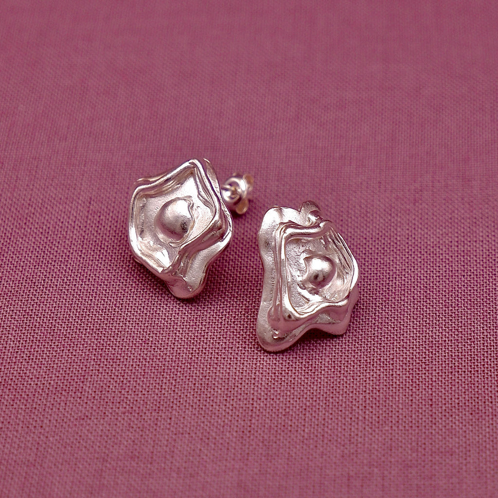 Silver shaped earrings on a pink fabric background
