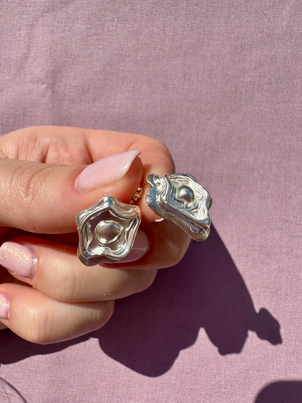 Silver rings designs held by a hand against a pink background