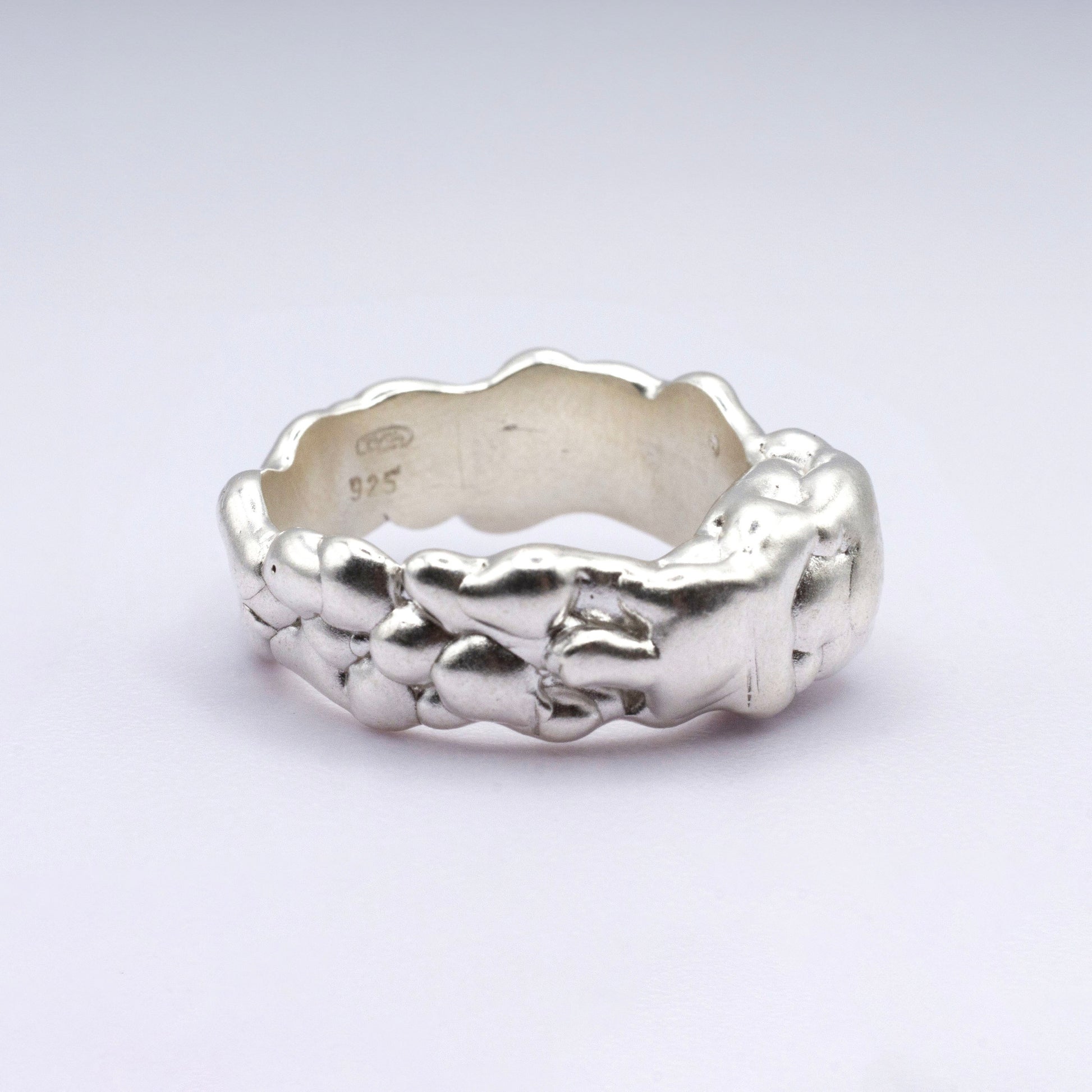 Silver ring with textured design on a light gray background