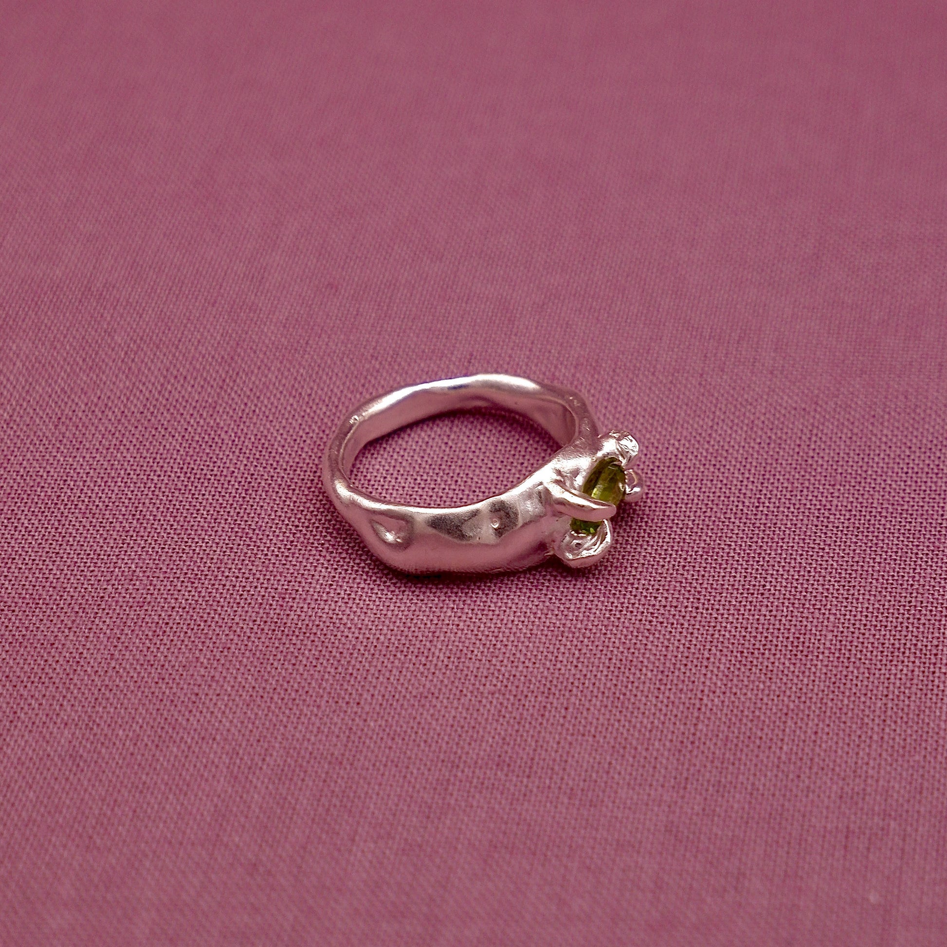 Silver ring with a green gemstone on a pink fabric background