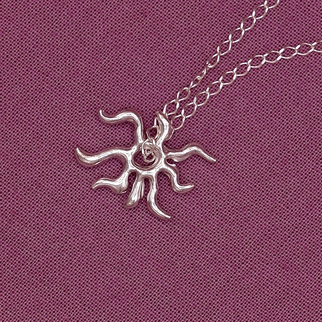 Silver sun-shaped pendant on a chain against a purple fabric background