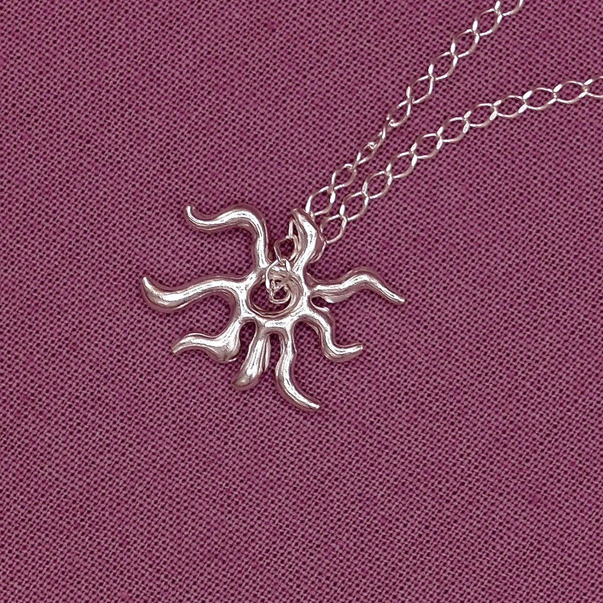 Silver sun-shaped pendant on a chain against a purple fabric background