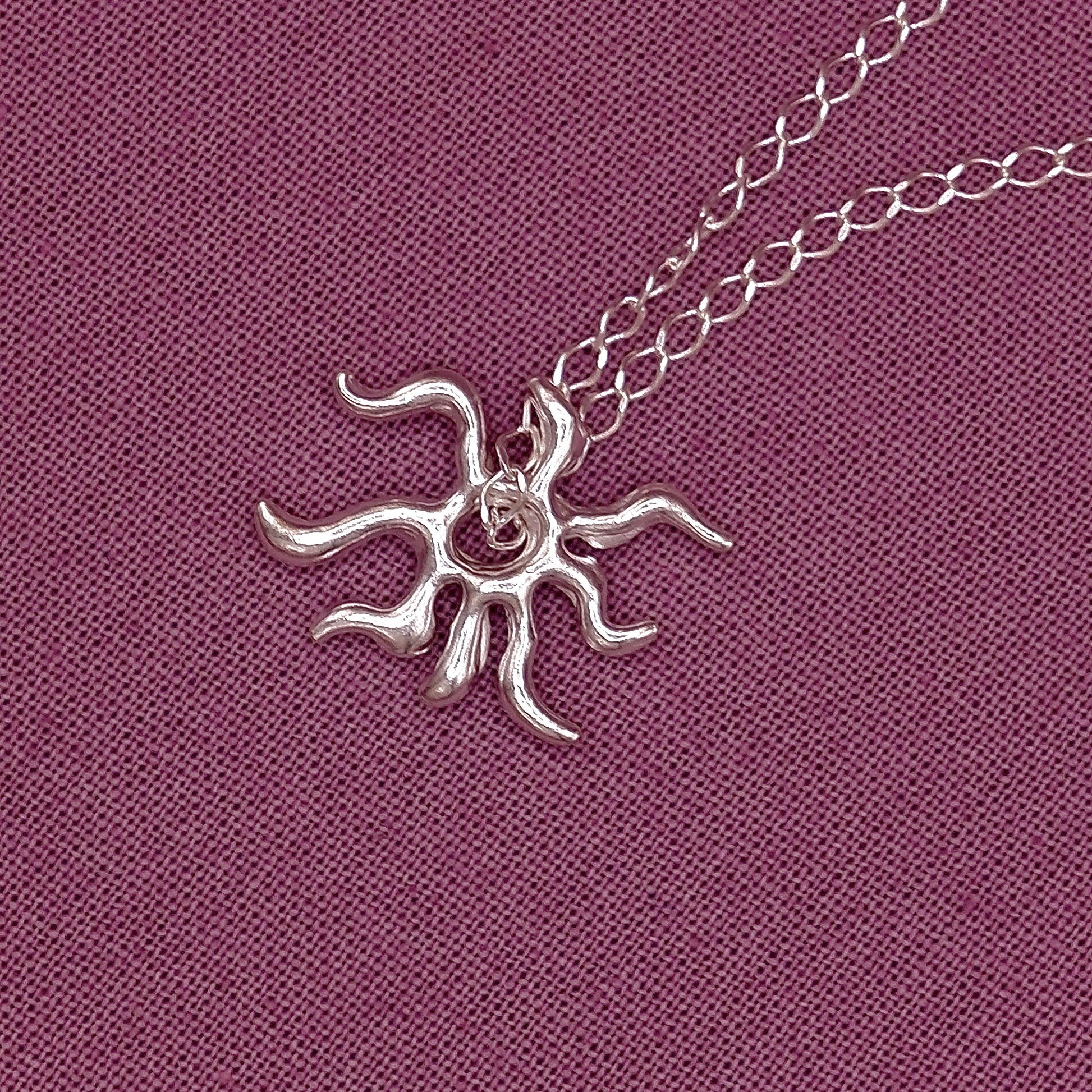 Silver sun-shaped pendant on a chain against a purple fabric background