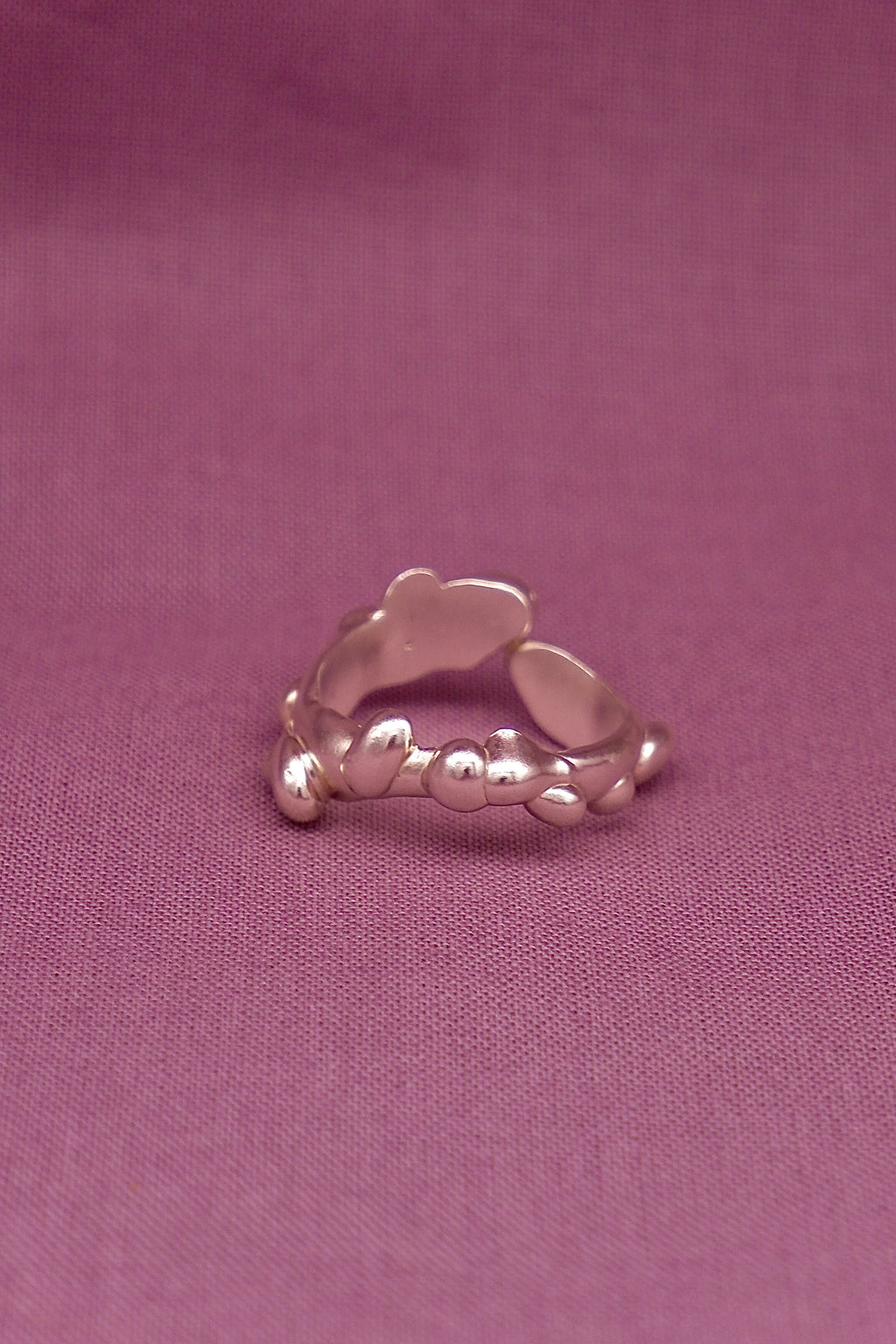 Silver ring with a textured design on a purple fabric background
