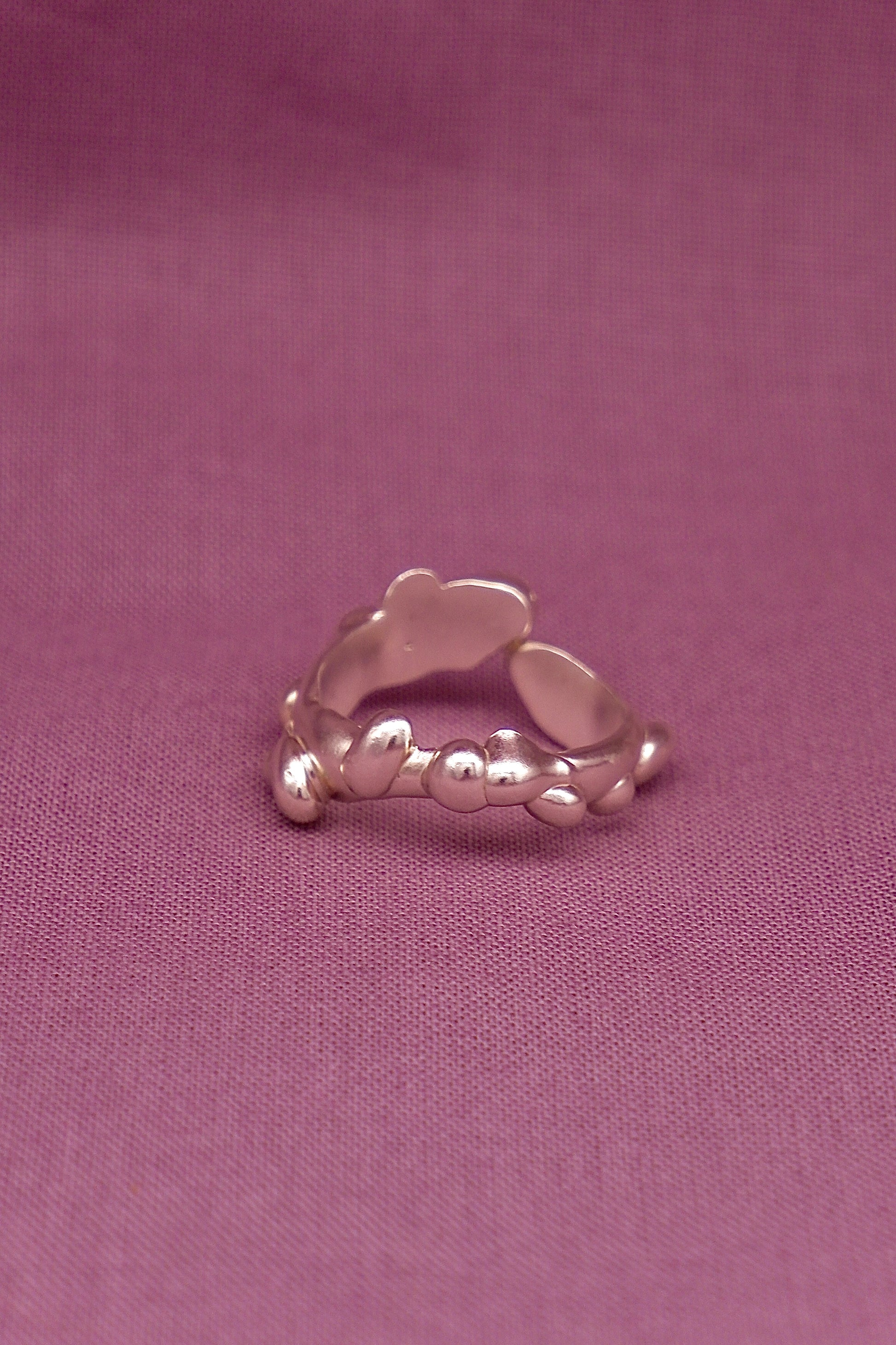 Silver ring with a textured design on a purple fabric background