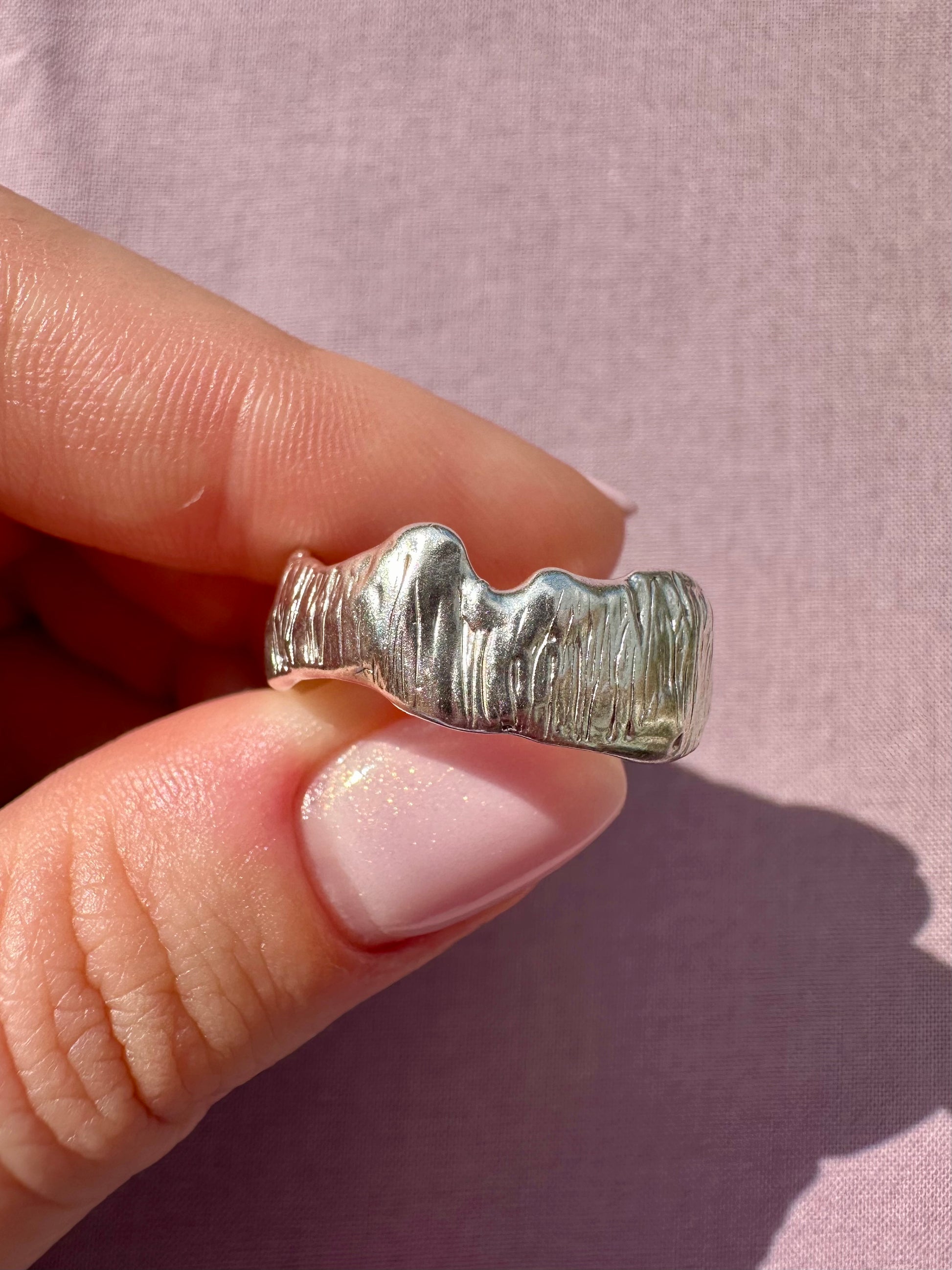 Silver ring being held on a pink background