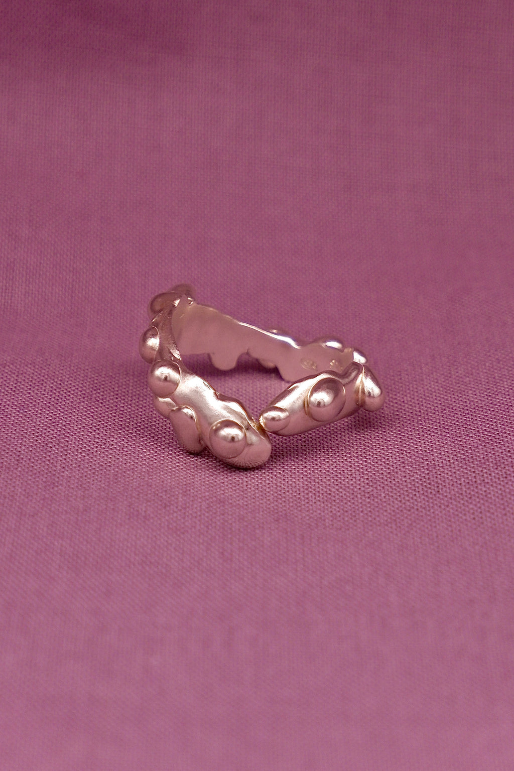 Silver ring with a textured band on a pink background