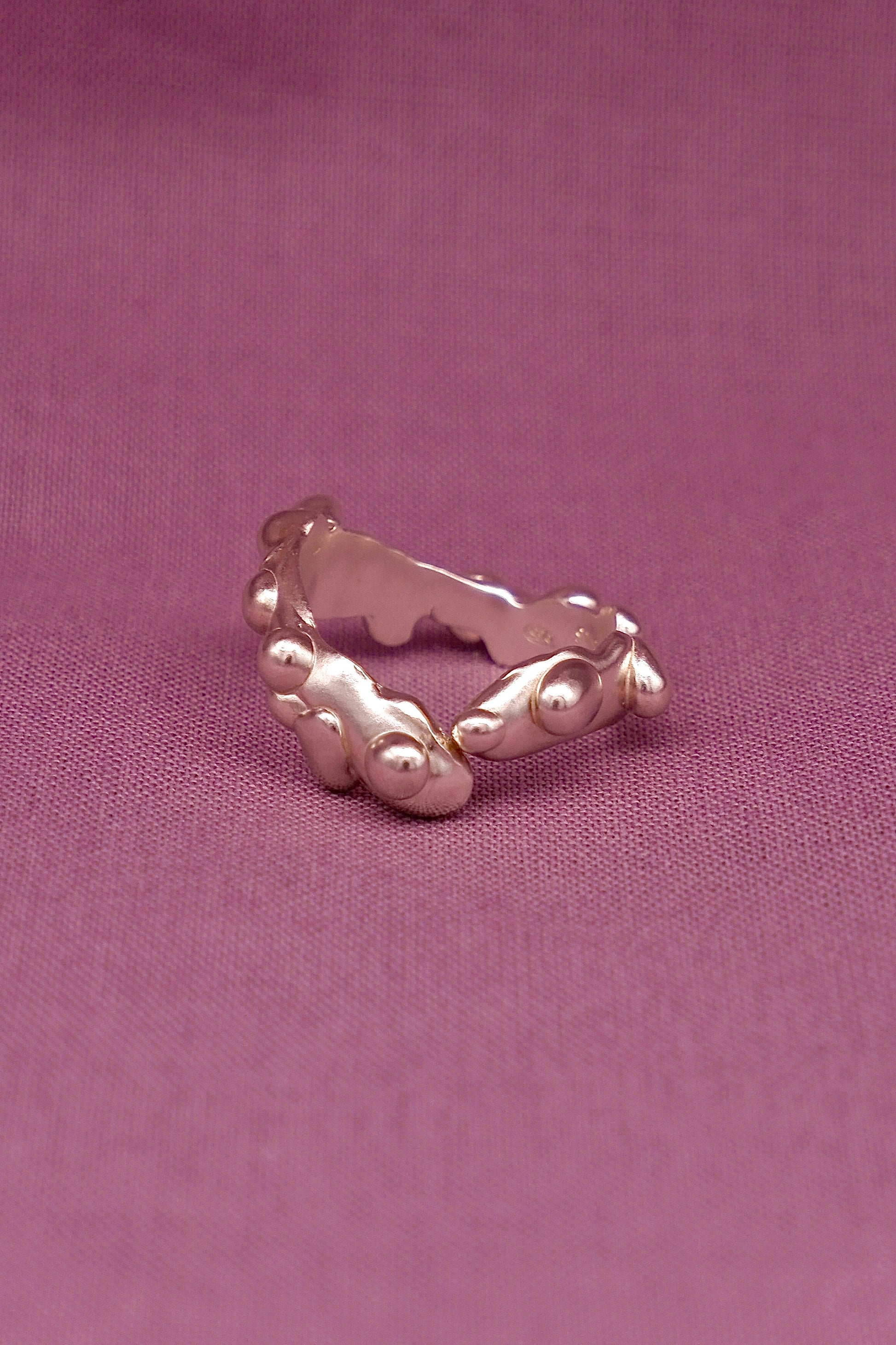 Silver ring with a textured band on a pink background