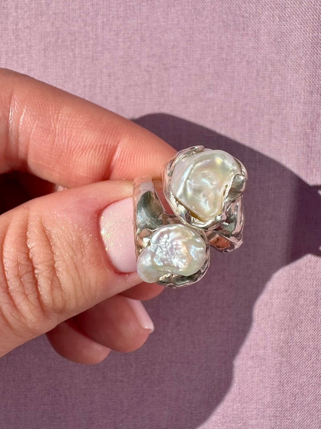 Silver ring with pearl  stones held by a hand against a pink background