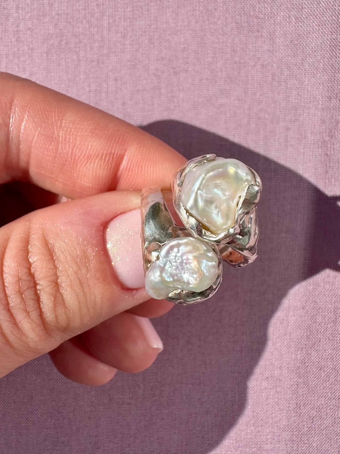 Silver ring with pearl  stones held by a hand against a pink background